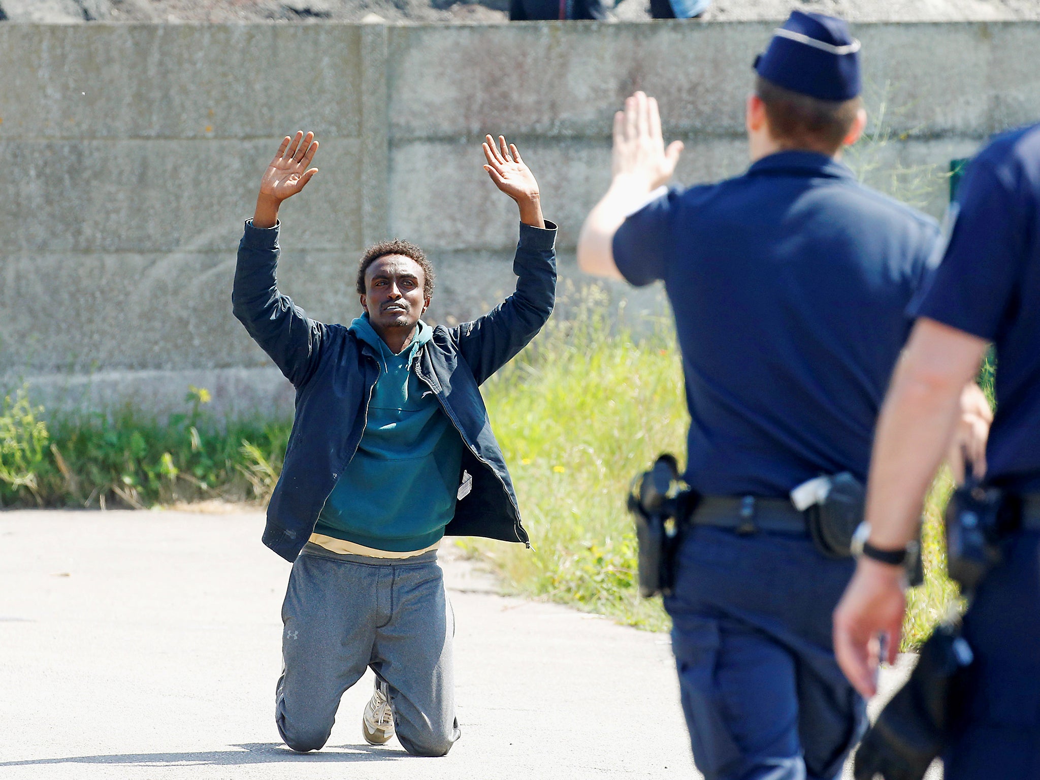 French riot police signal to a migrant who is on his knees as French authorites block their access to a food distribution point in Calais, France