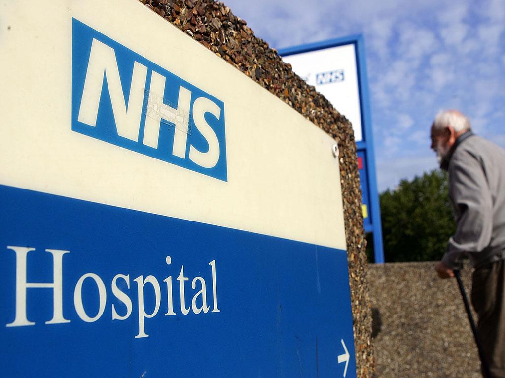 An elderly gentleman walks past a hospital sign