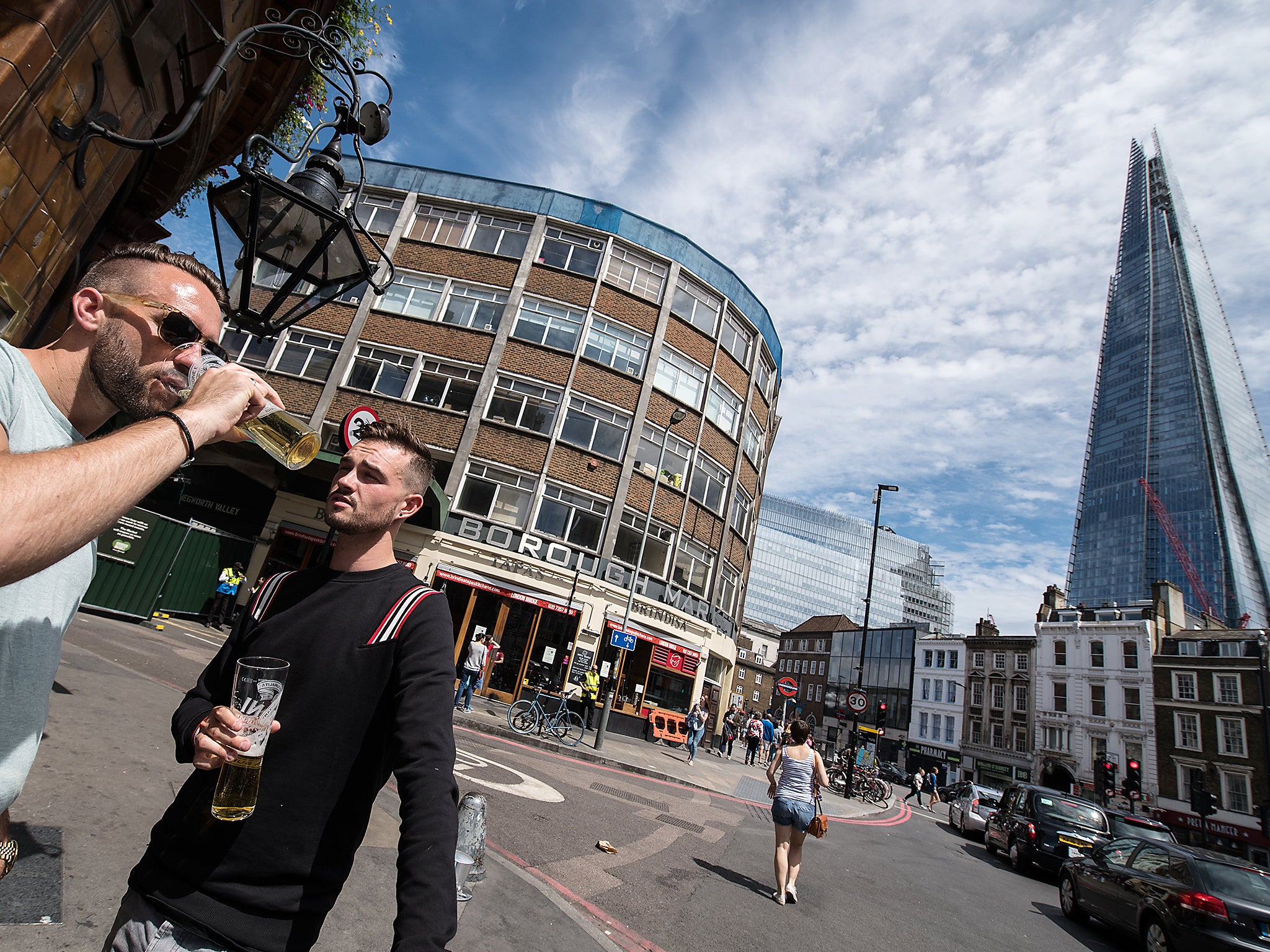 Two men drink beer outside the Southwark Tavern which reopened for business today next to an entrance to Borough Market which remains closed in London