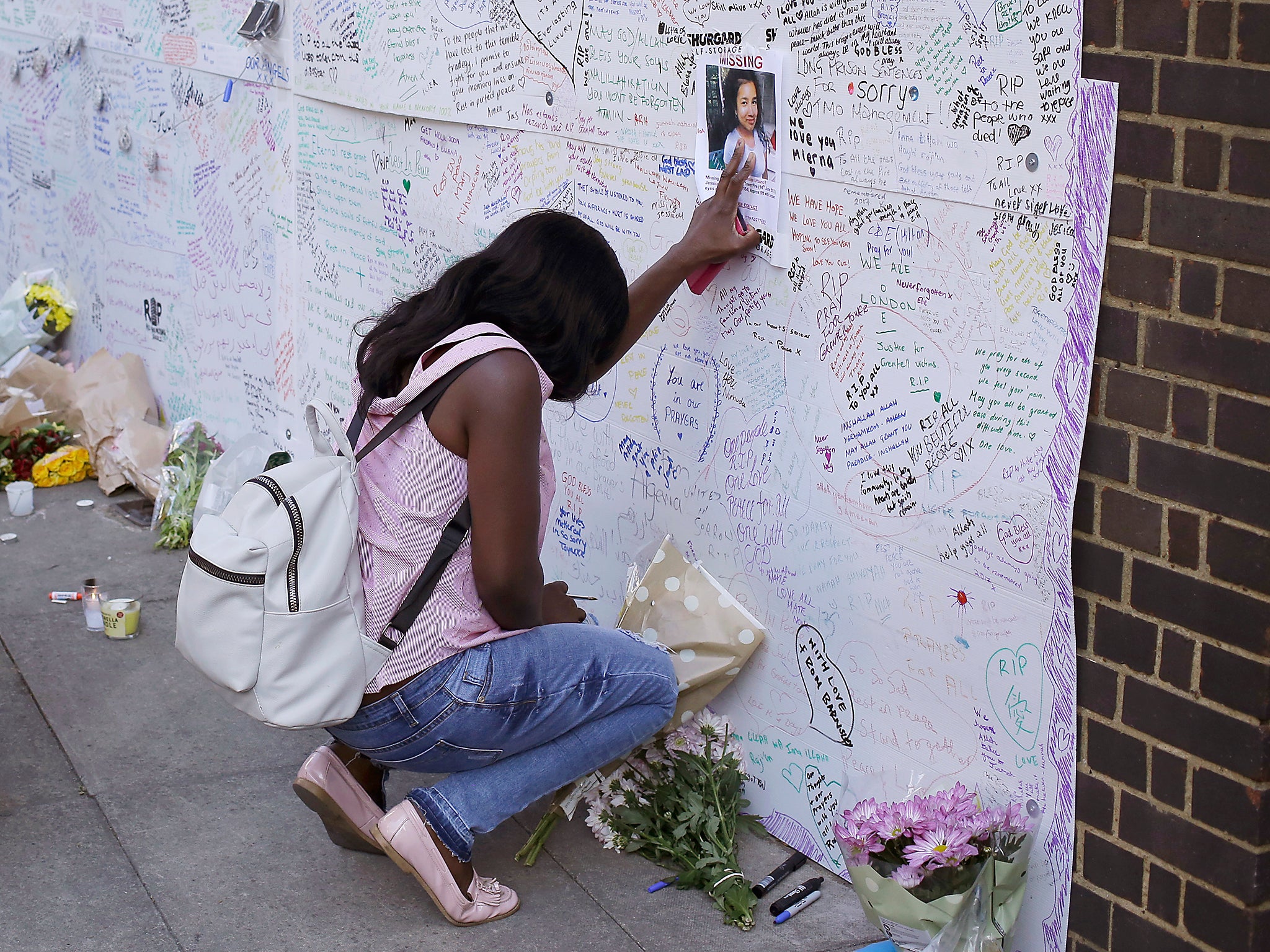 A woman touches a missing poster for 12-year-old Jessica Urbano on a tribute wall after laying flowers on the side of Latymer Community Church next to Grenfell Tower