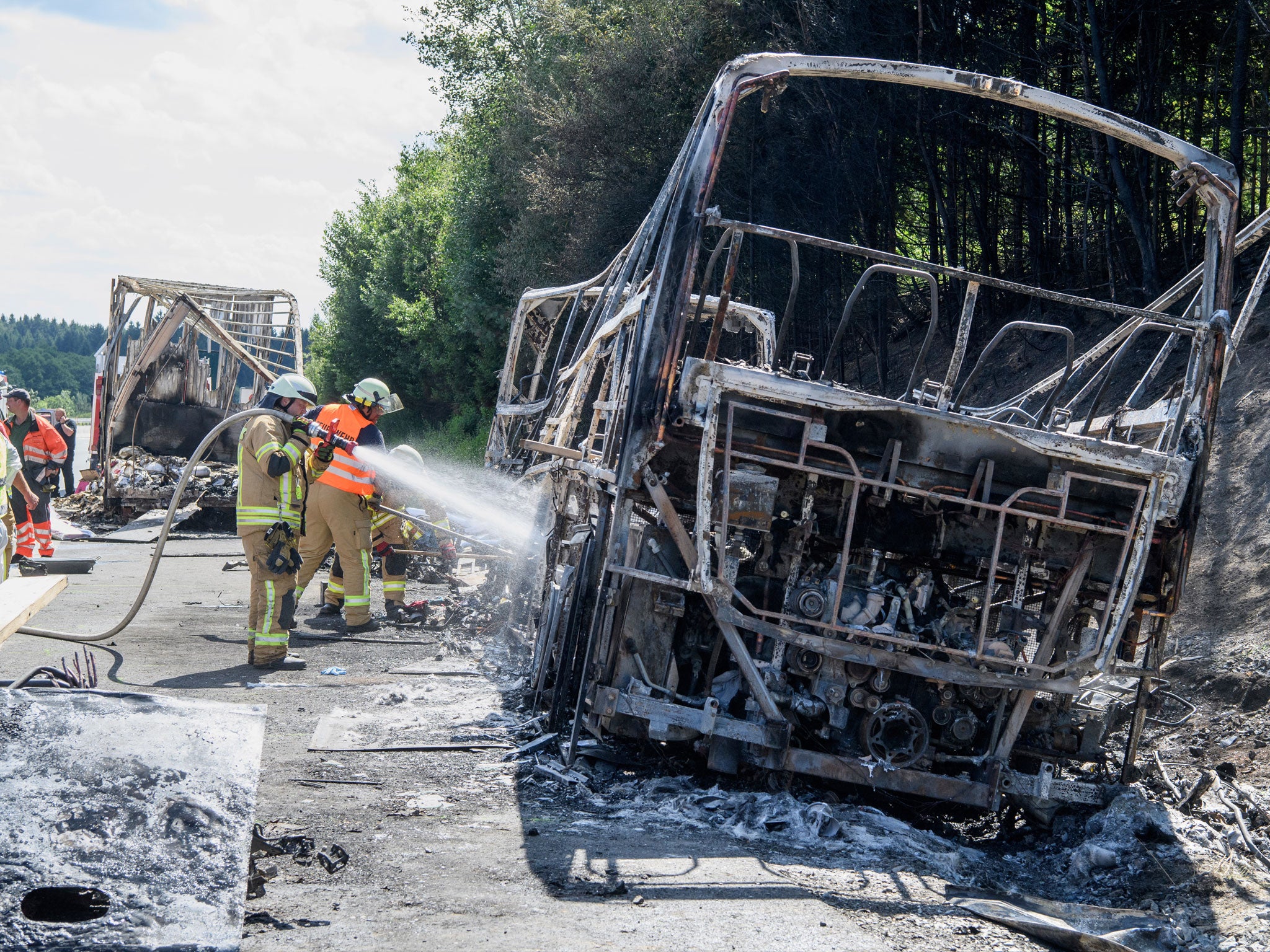 Firefighters work on the wreckage of the burnt-out bus