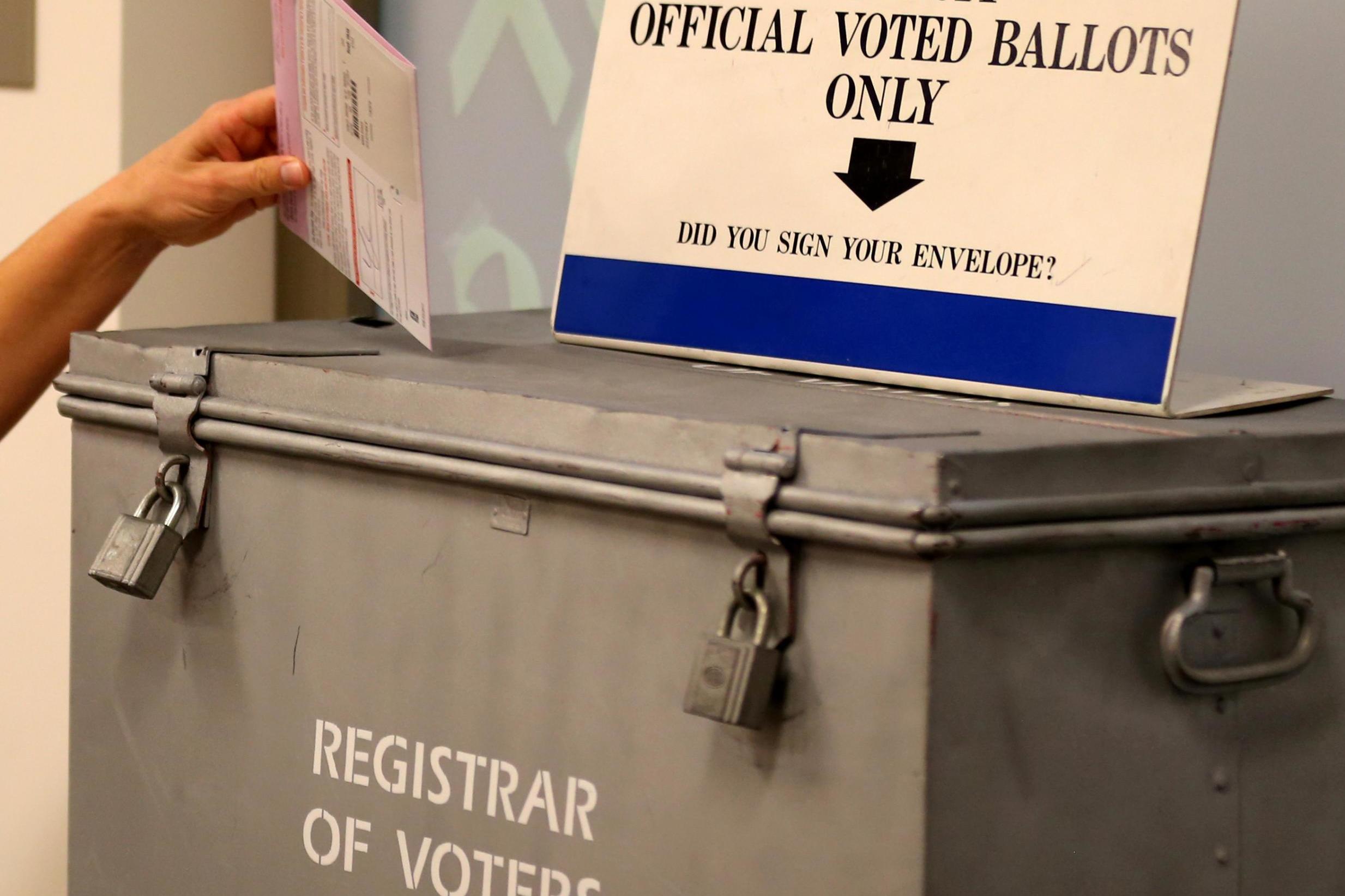 A ballot is placed into a locked ballot box by a poll worker as people line-up to vote early at the San Diego County Elections Office in San Diego, California