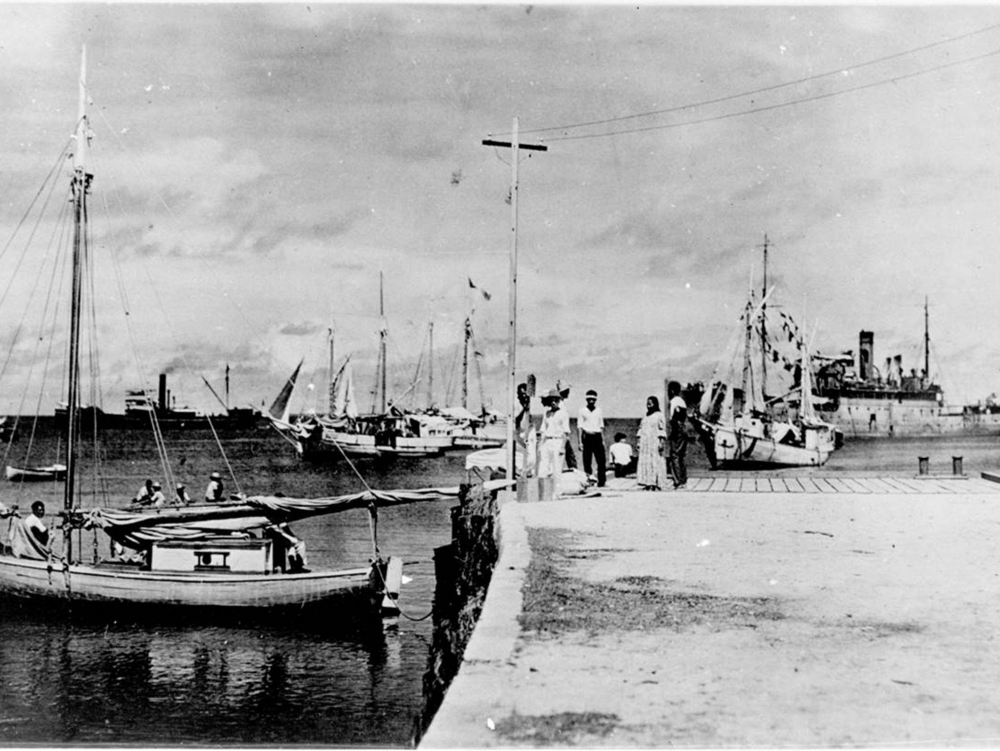 The photograph shows a short-haired woman sitting on a dock, alongside a man who appears to have a similar hairline to Fred Noonan, her navigator on that fateful flight