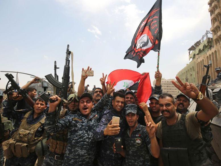 Members of the Iraqi federal police dance and wave their country's national flag in celebration in the Old City of Mosul on July 8, 2017