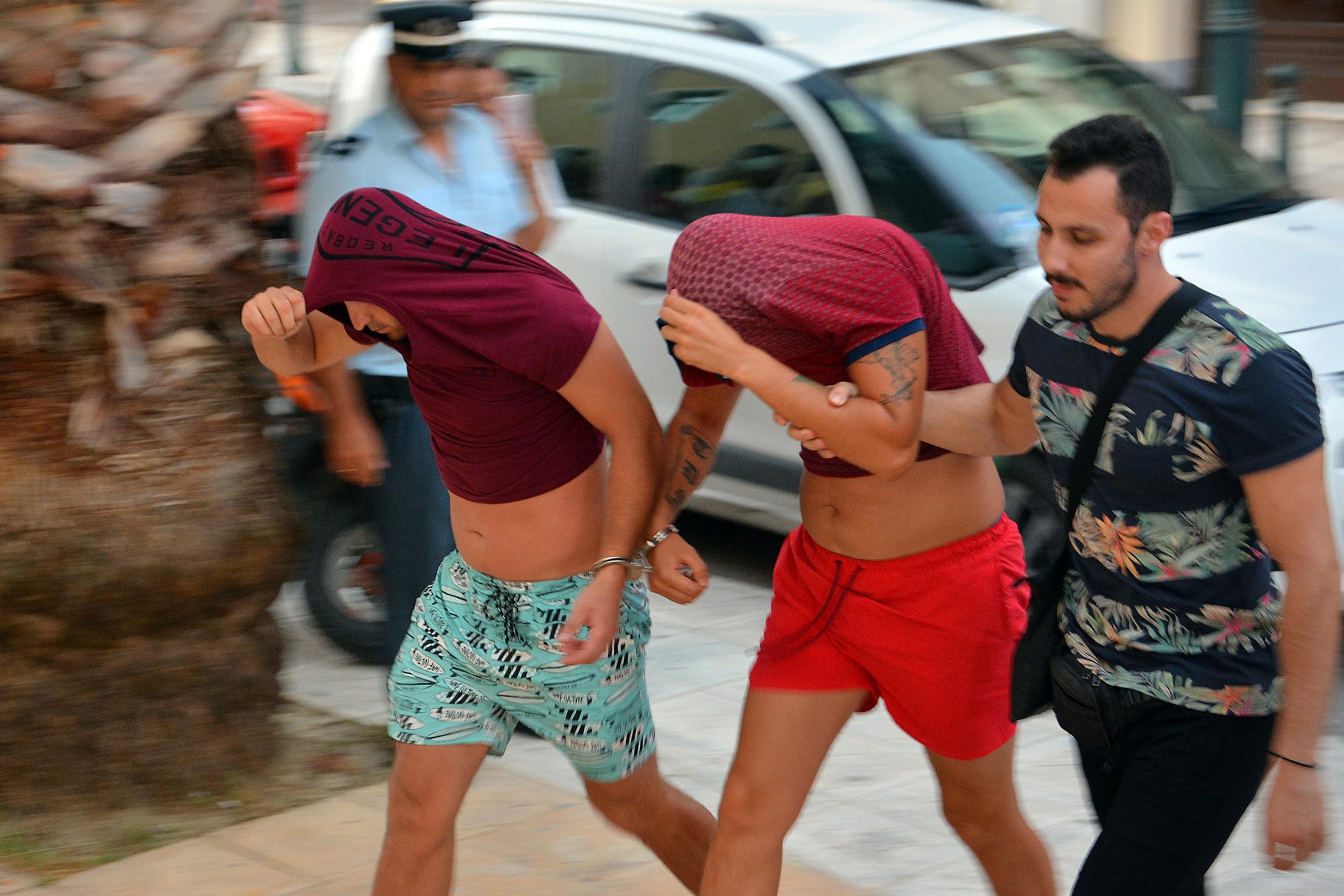 Greek police escort suspects with their heads covered to the Zakynthos prosecutor's office to face charges over the killing of a Bakari Henderson