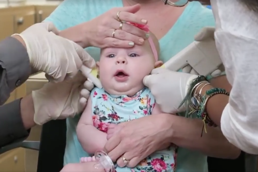 Two workers puncture the baby’s lobes at the same time using a piercing gun