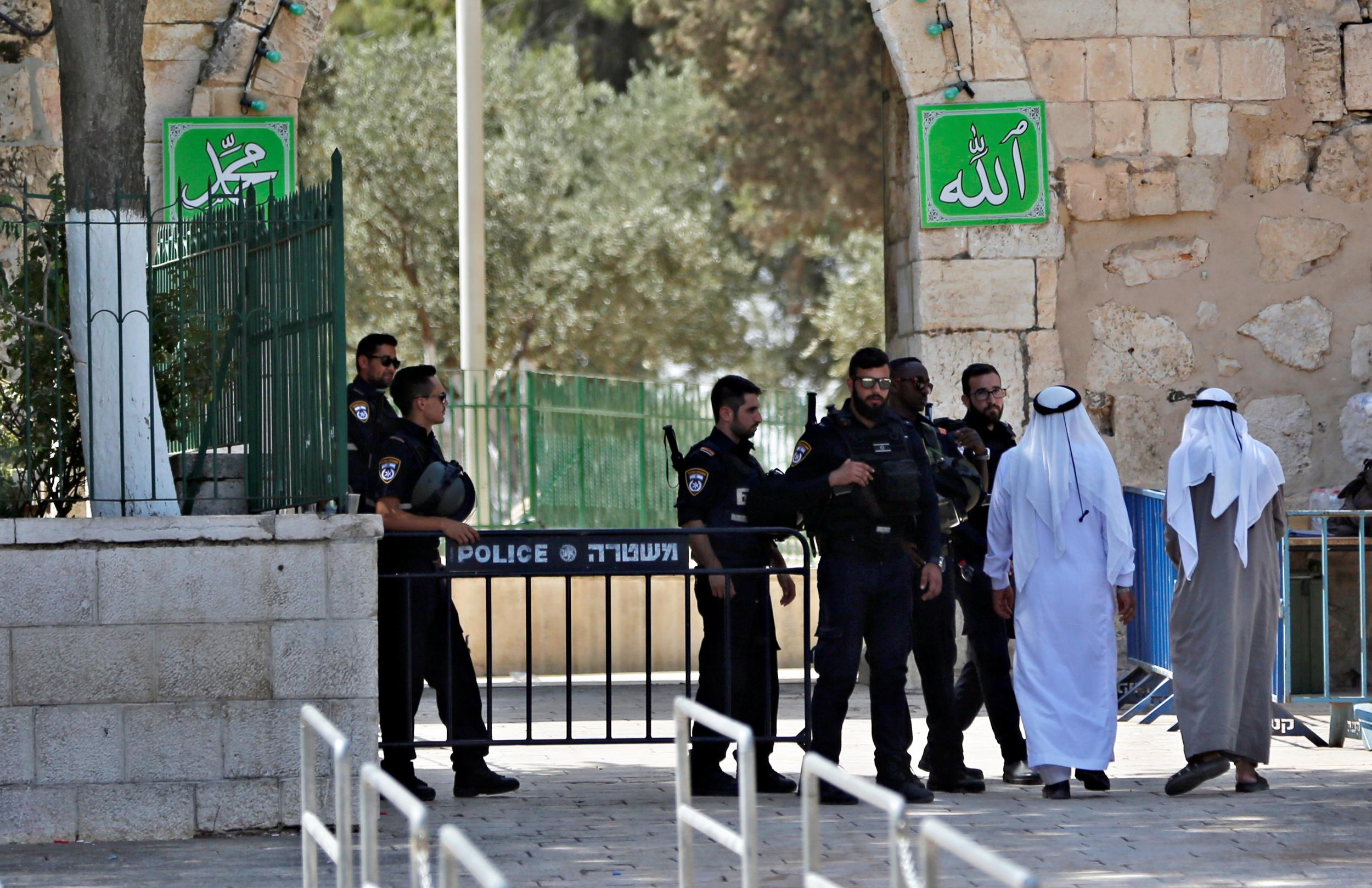 Palestinians walk next to Israeli security forces at the entrance of the compound