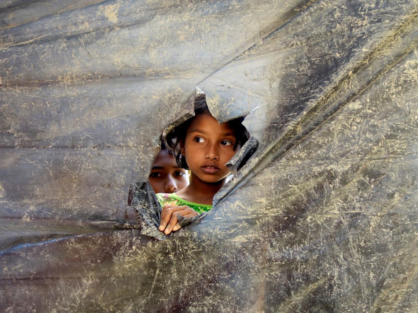 A Rohingya refugee girl peeks through a hole made in a plastic wall dividing the shelters at Balu Kali Refugee Camp in Cox's Bazar, Bangladesh, 28 February, 2017