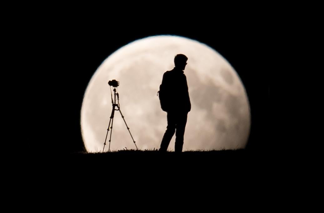 A man takes pictures of the moon standing in a partial lunar eclipse on August 7