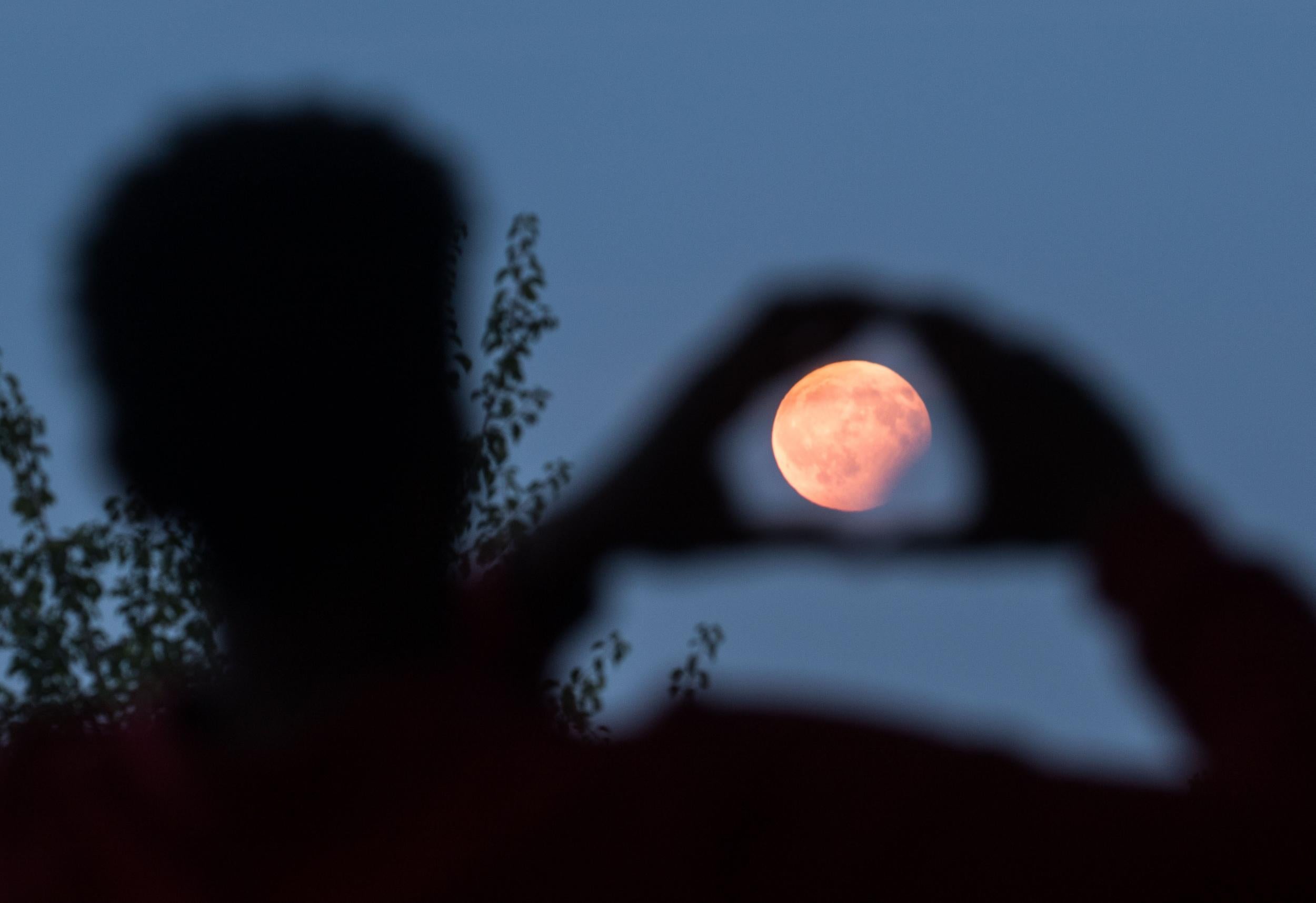 A man frames with his hands the moon standing in a partial lunar eclipse on August 7, 2017 in Frankfurt am Main, western Germany