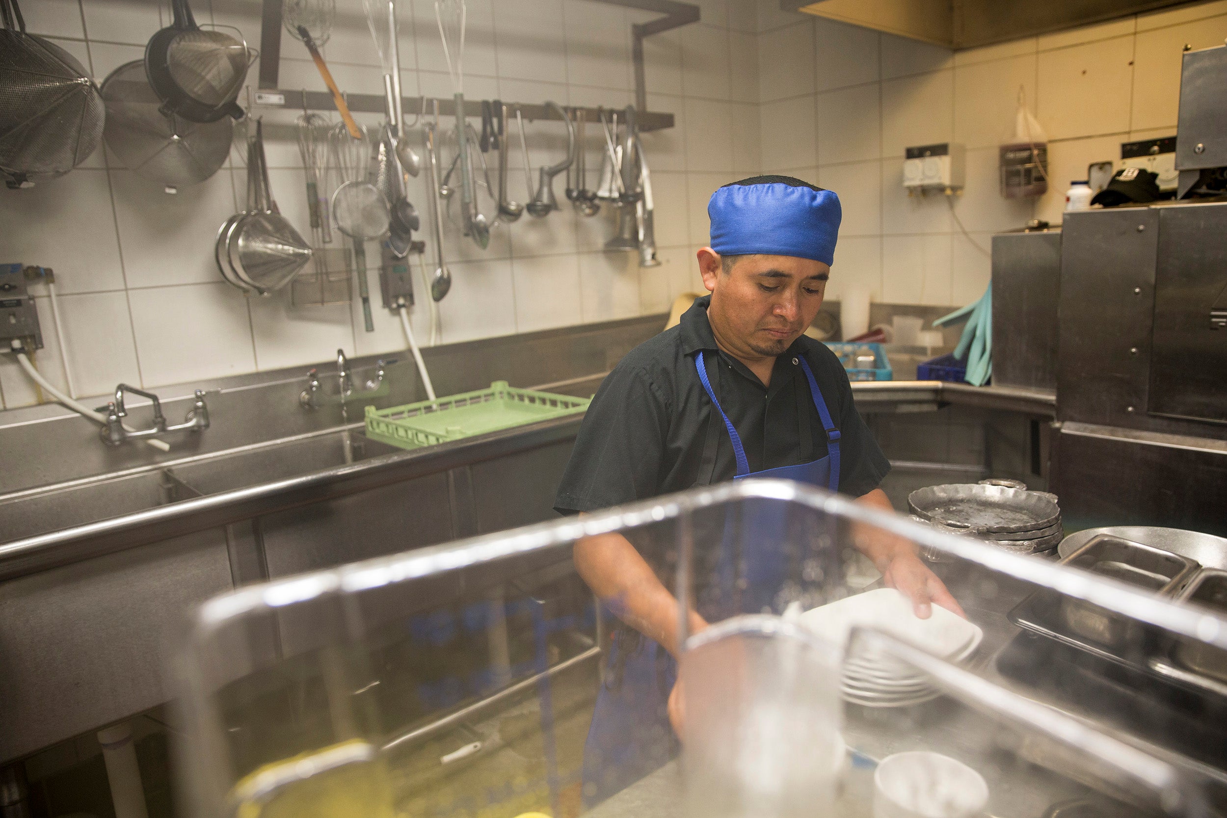 Pot washer Esteban Soc is stacking plates while working in the kitchen at Caracol