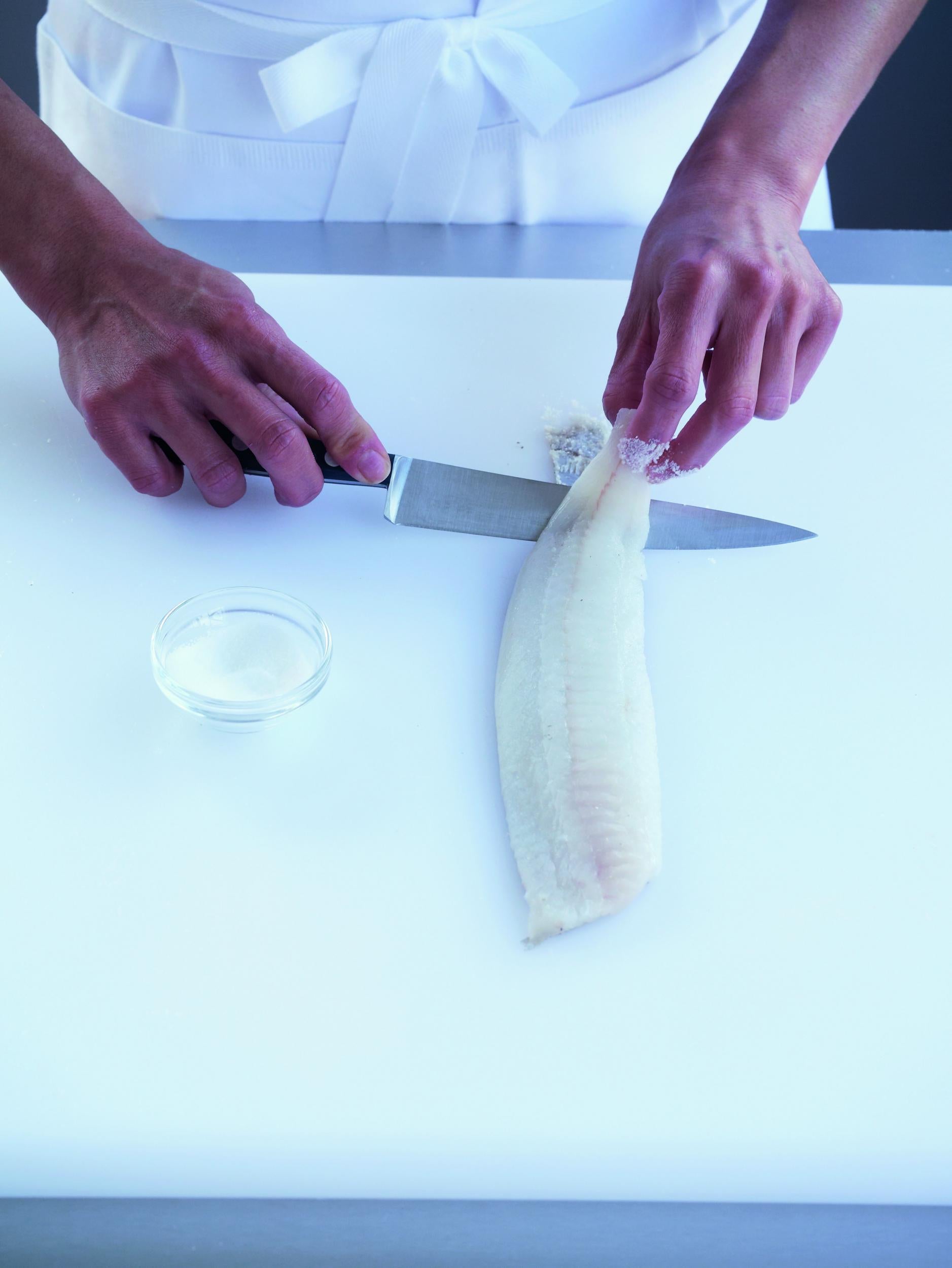 2. Holding the narrow end of the fillet firmly and inserting the knife at an angle between the skin and the fillet