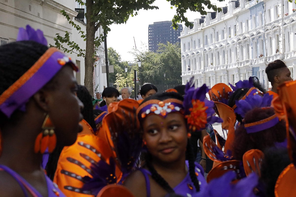 The burned-out shell of the Grenfell tower block overlooks carnival performers at the Notting Hill Carnival in west London