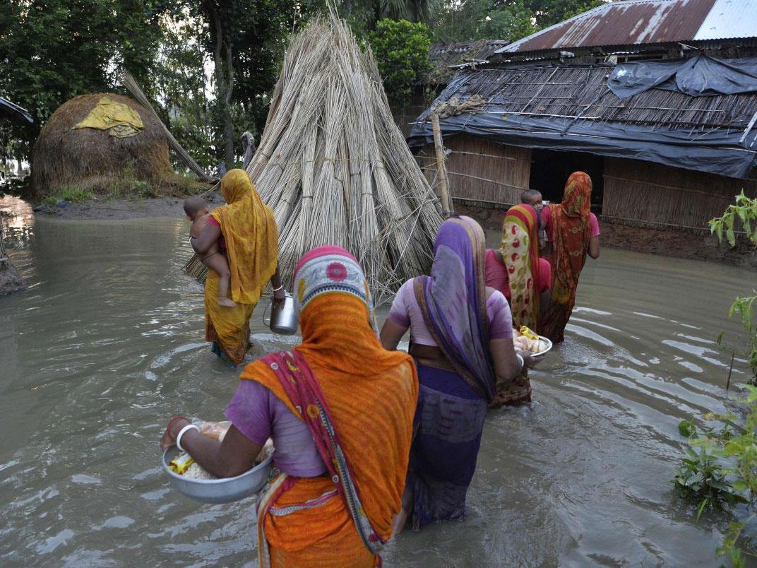 Cillagers wade through flood waters after collecting relief food near the submerged houses in Gazole village at Malda district in the Indian state of West Bengal