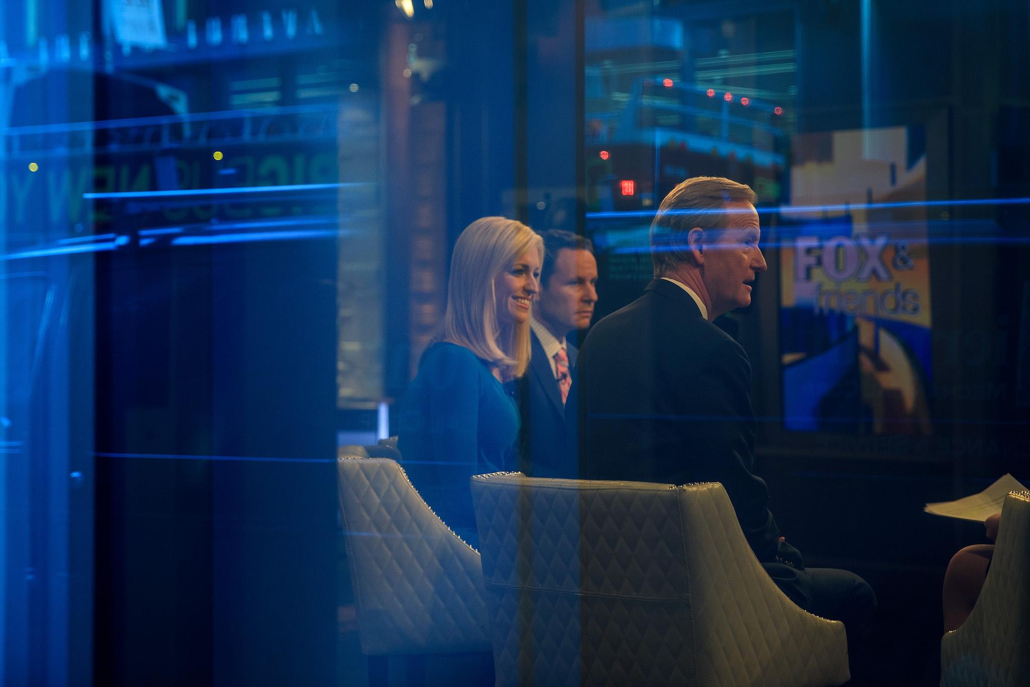 Seen through a window, hosts Brian Kilmeade, Ainsley Earhardt, and Steve Doocy broadcast 'Fox And Friends' from the Fox News studios