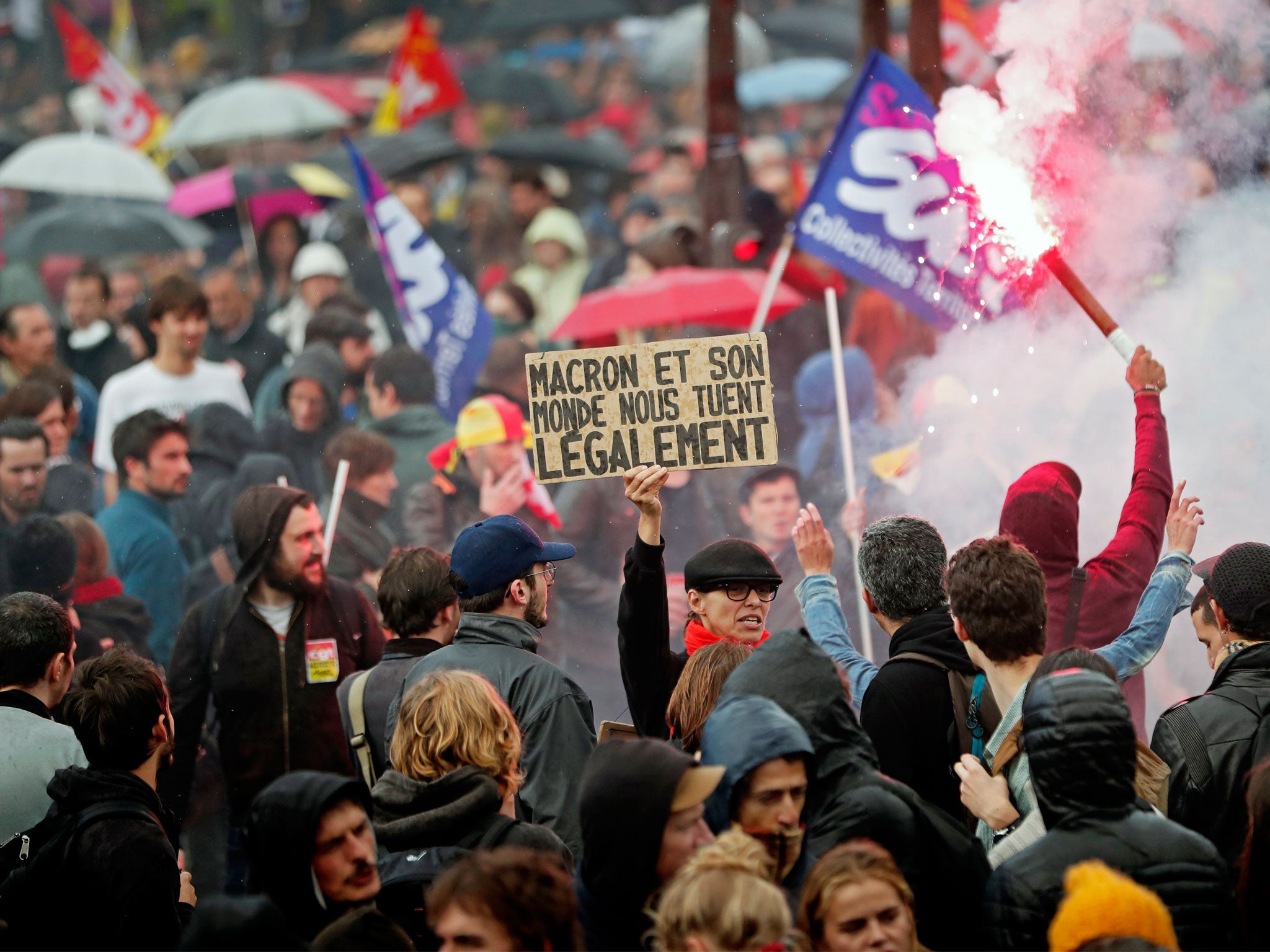 A demonstrator holds a poster reading 'Macron and his world are legally killing us' as thousands of protesters gathered in Paris