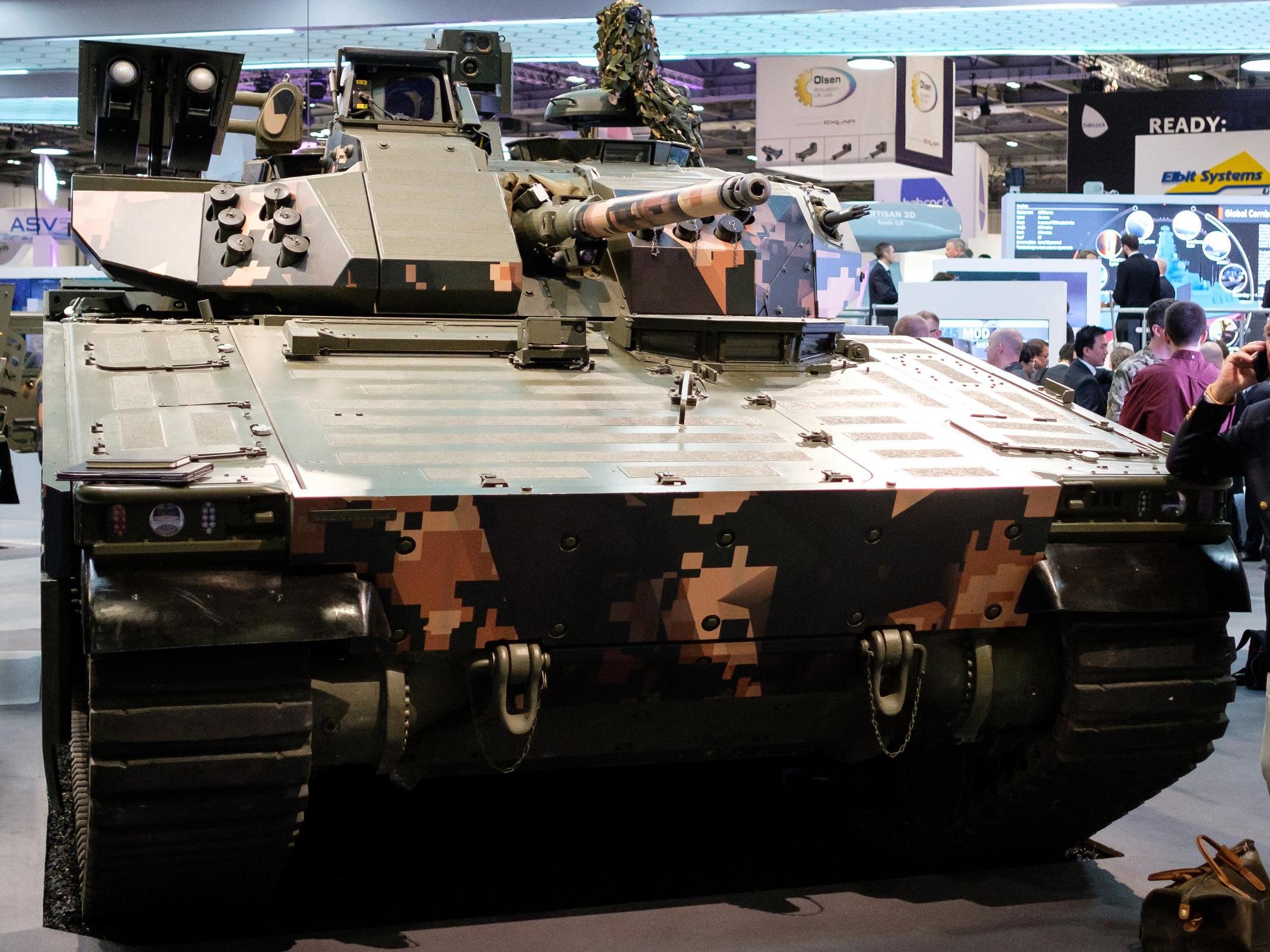 A man chats on his phone as he leans on a CV90 Battle Station in the BAE Systems display area