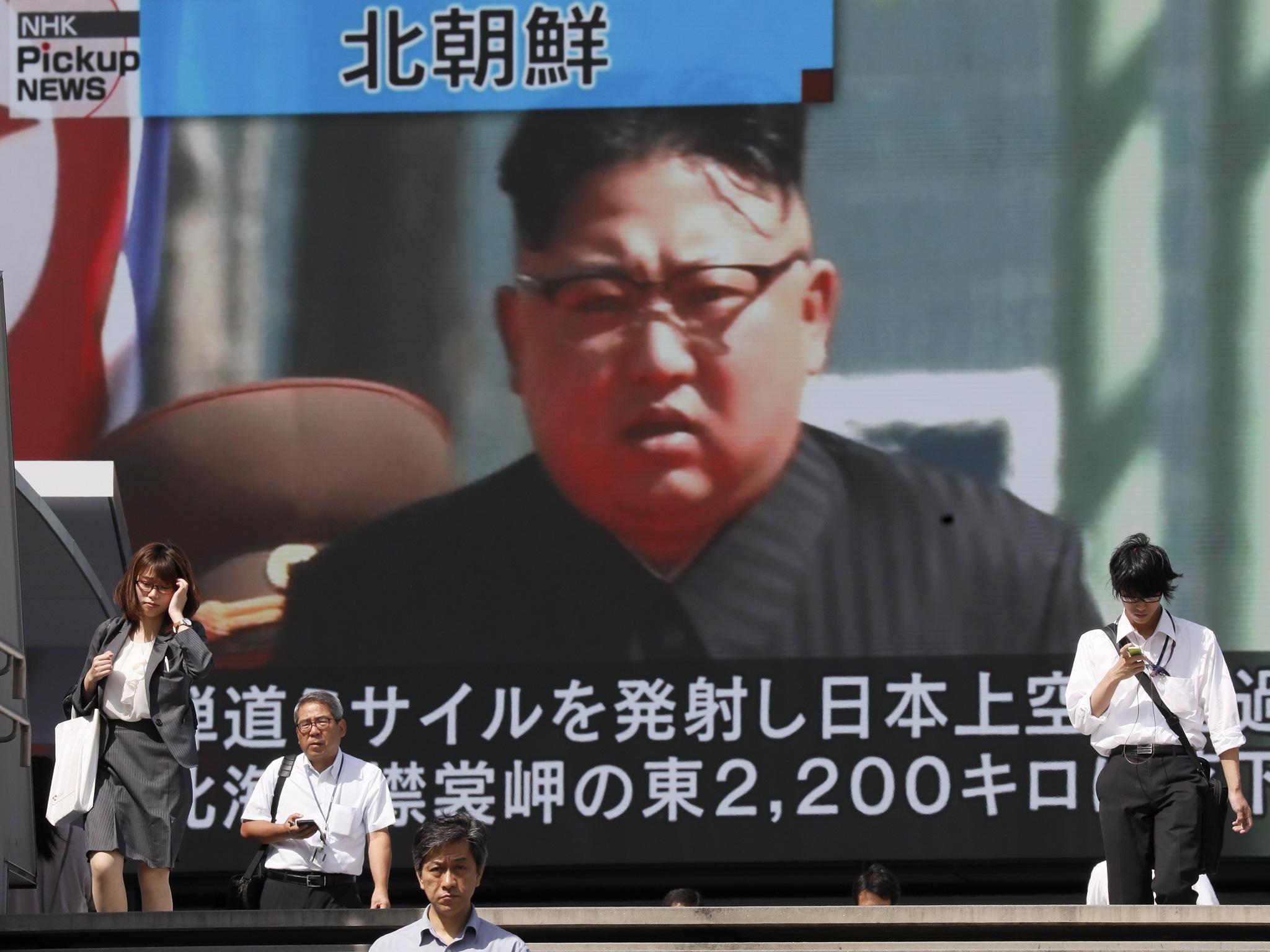 Pedestrians walk under a large-scale monitor displaying North Korean leader Kim Jong-un on a TV news broadcast in Tokyo, Japan