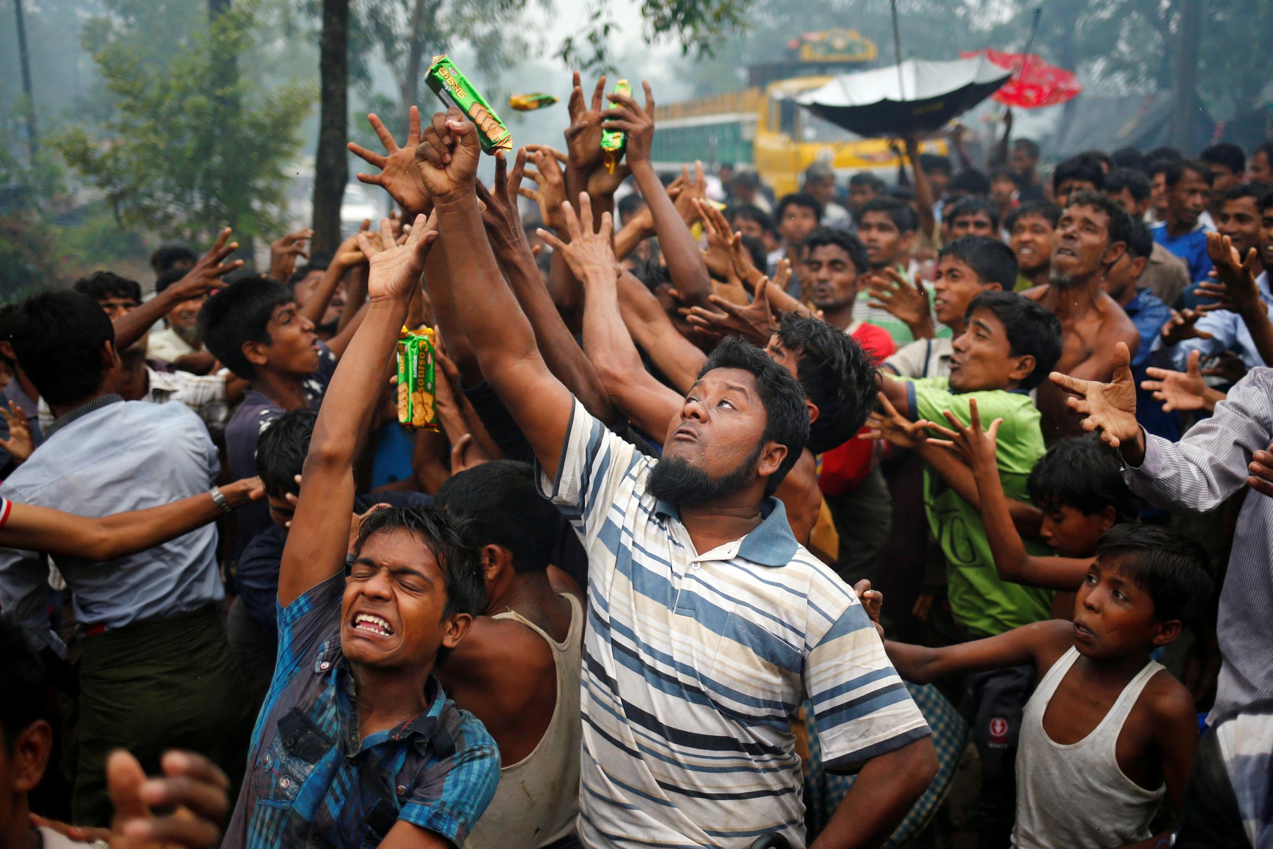 Rohingya refugees reach out their hands to grab aid packages at a refuee camp in Cox's Bazar, Bangladesh