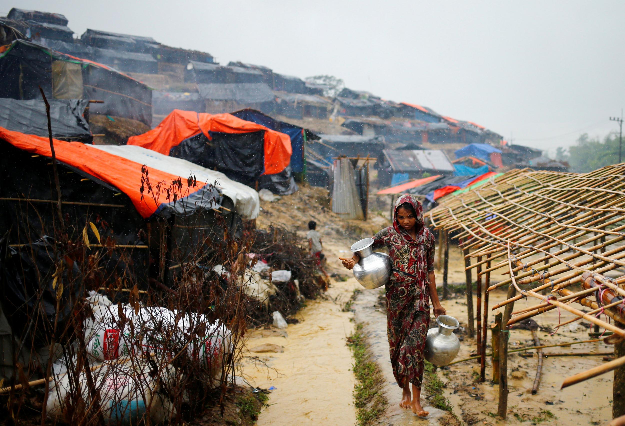 A Rohingya refugee woman carries water jars during rainy weather at a makeshift camp in Cox's Bazar, Bangladesh