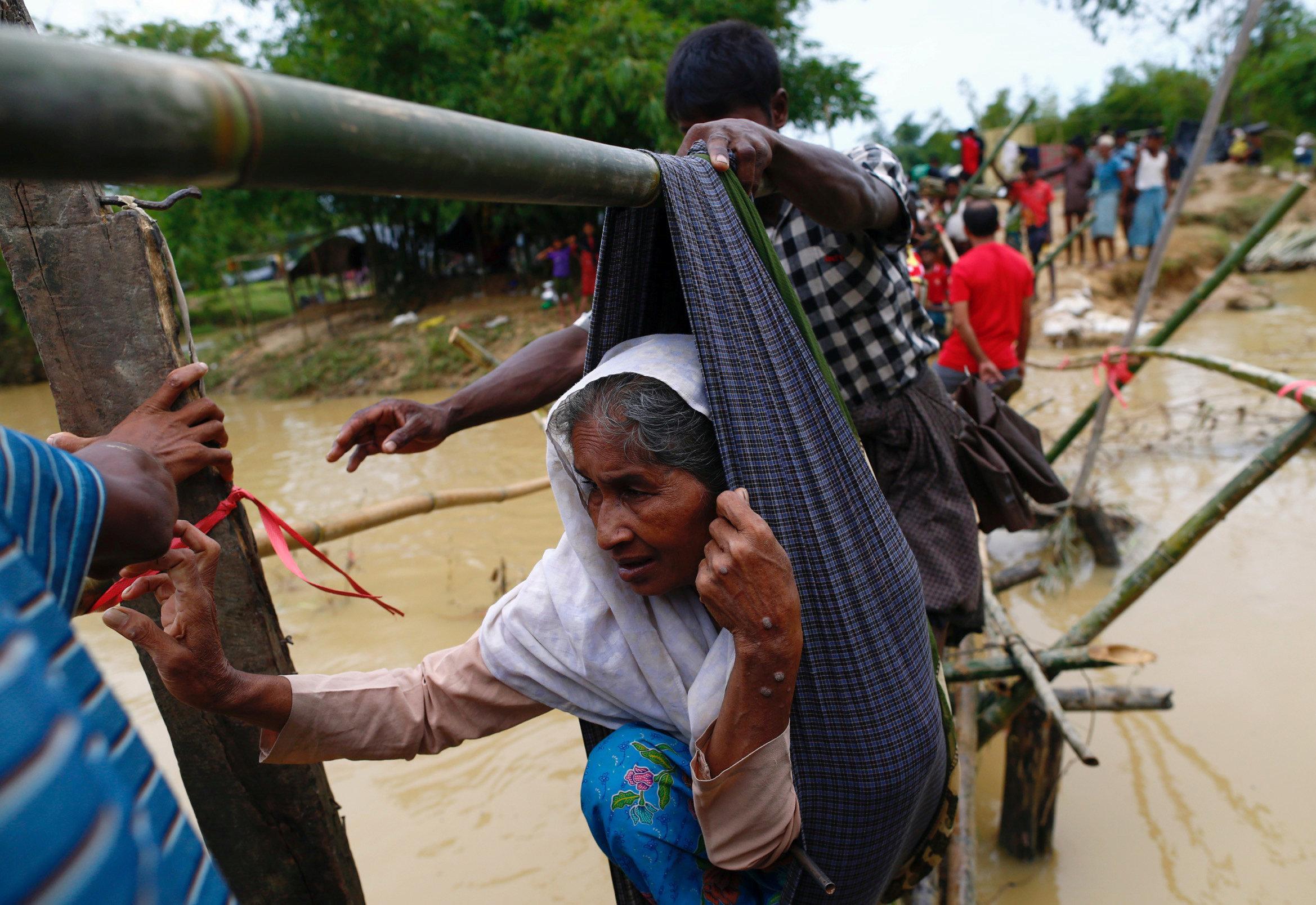 A Rohingya refugee woman is carried in a sling, through a swollen water stream in Cox's Bazar, Bangladesh