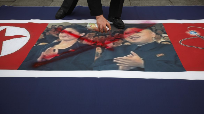 An activist from an anti-North Korea civic group defaces a North Korea flag depicting North's leader Kim Jong-un and his wife Ri Sol-ju during a rally against North Korea's nuclear test near the US embassy in central Seoul on 12 February, 2013 (Reuters)