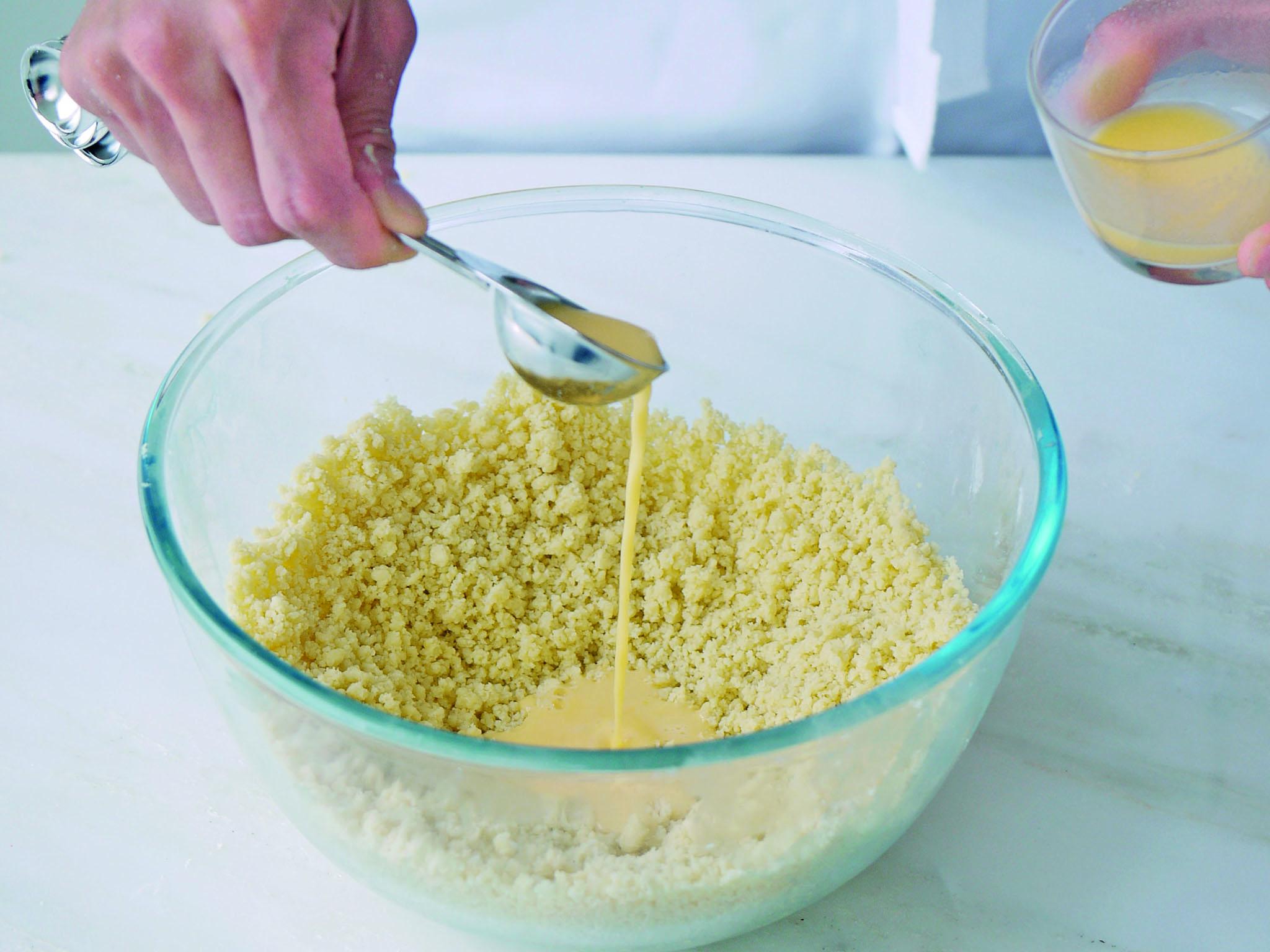 5. Mix the egg yolks and water together in a small bowl with a fork until evenly combined. Add 2 tbsp of the yolk mixture to the crumb and, using a cutlery knife, distribute the liquid as quickly as possible (this will create flakes of pastry)