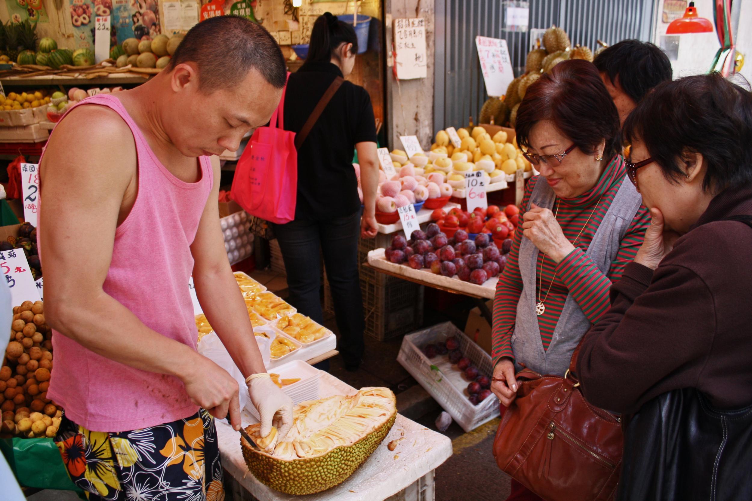 Two women in Hong Kong purchase some fleshy lobes of Jackfruit as a man extracts them from the fibrous shell