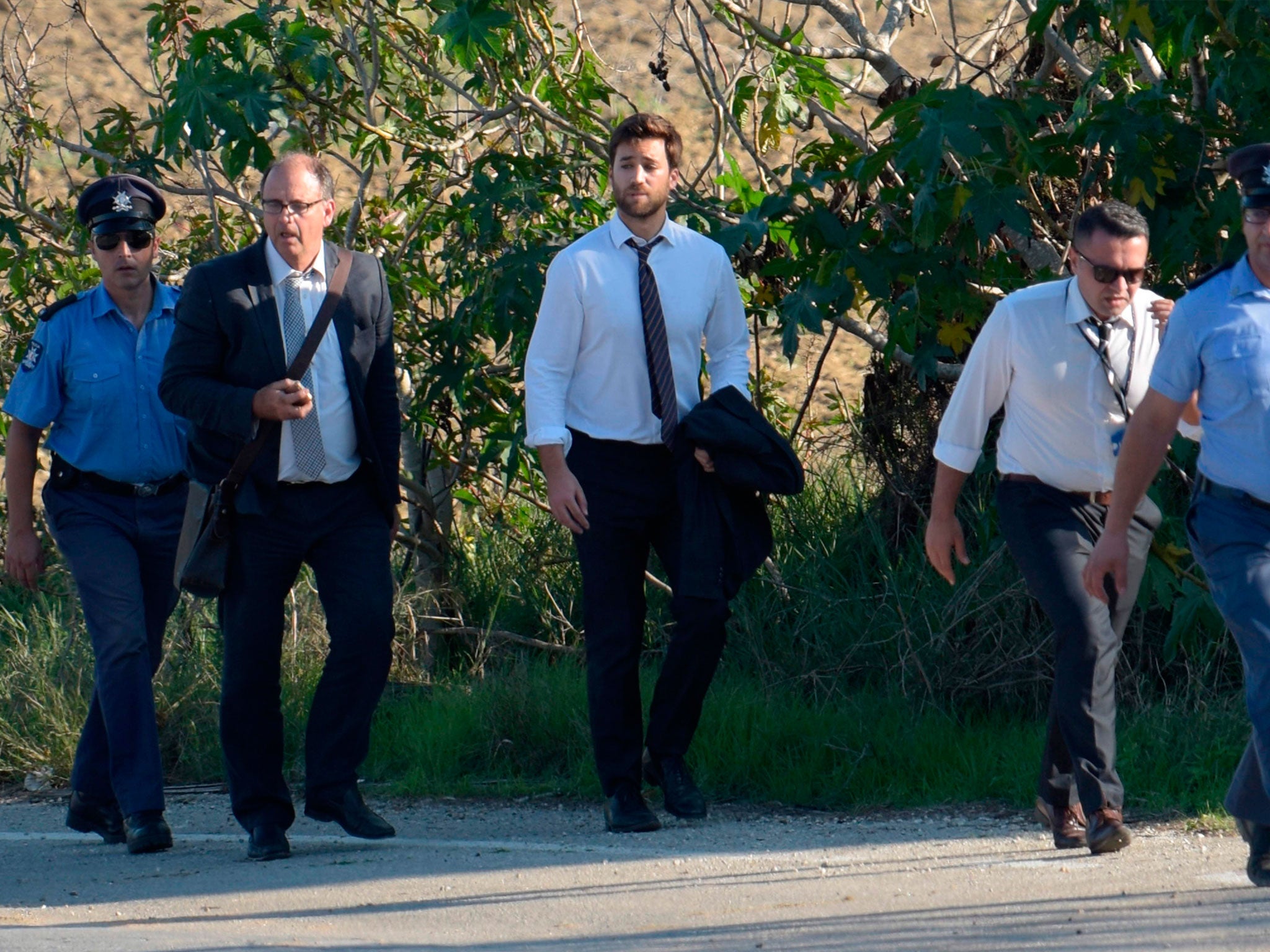 Matthew Caruana Galizia, middle, walks with policemen past the wreckage of a car bomb that killed Daphne Caruana Galizia close to her home in Bidnija, Malta