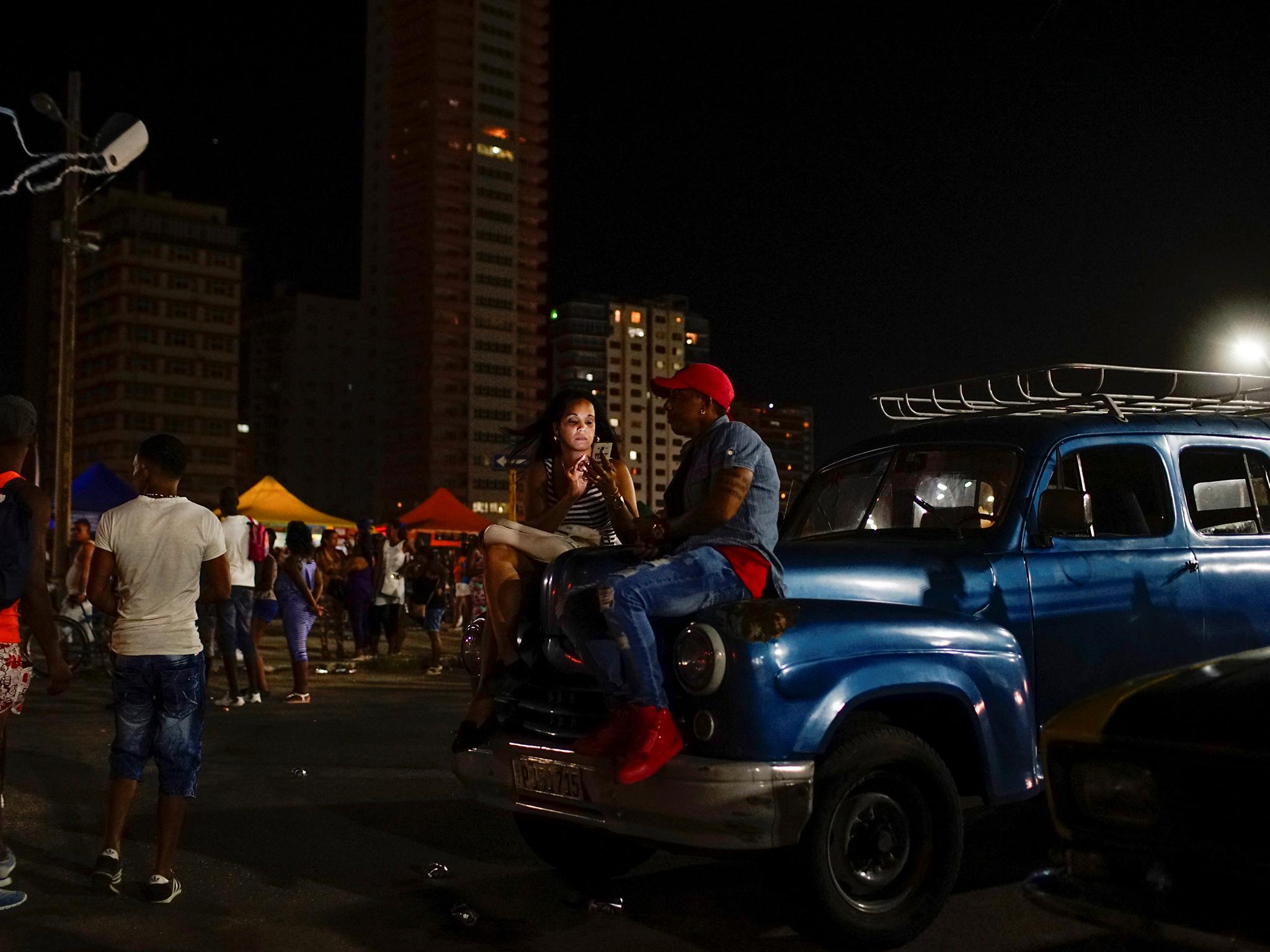 A woman sits on a vintage car as she uses a hotspot in Havana