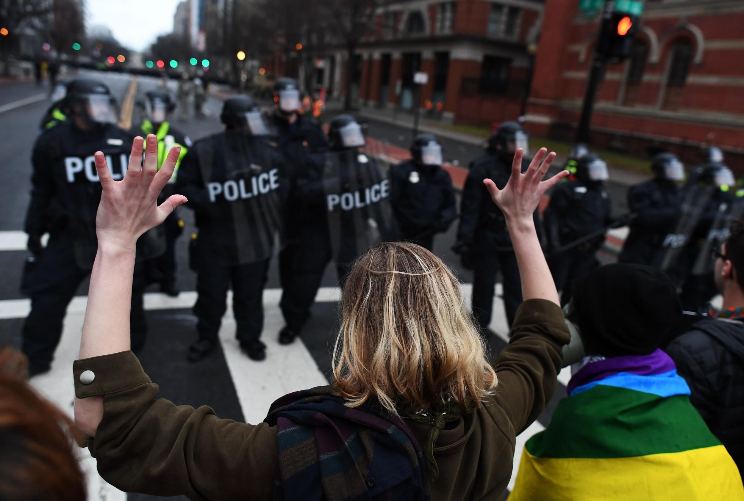 An anti-Trump protester holds her hands up as police officers line up in Washington DC, (Getty)