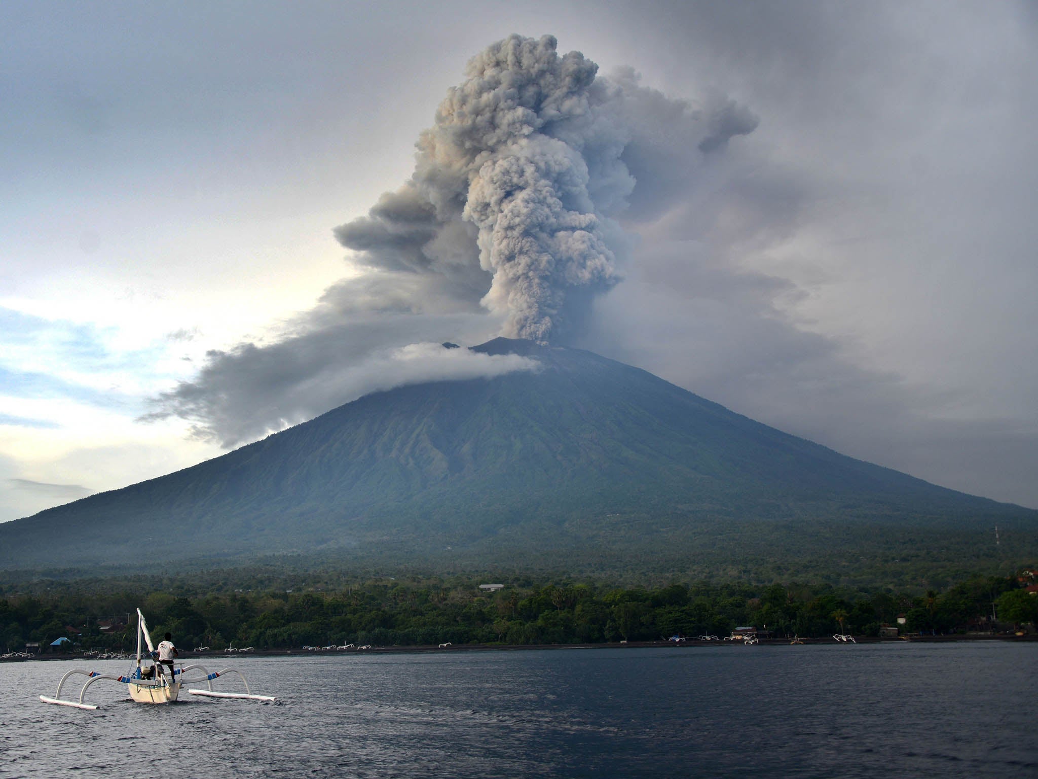 A fisherman drives a traditional boat as Mount Agung erupts (Getty)