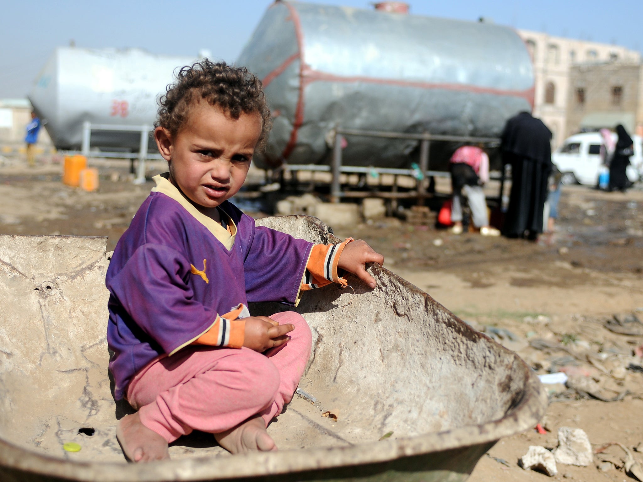 A Yemeni child sits on a wheelbarrow as he waits for his mother to fill their jerry cans with clean water