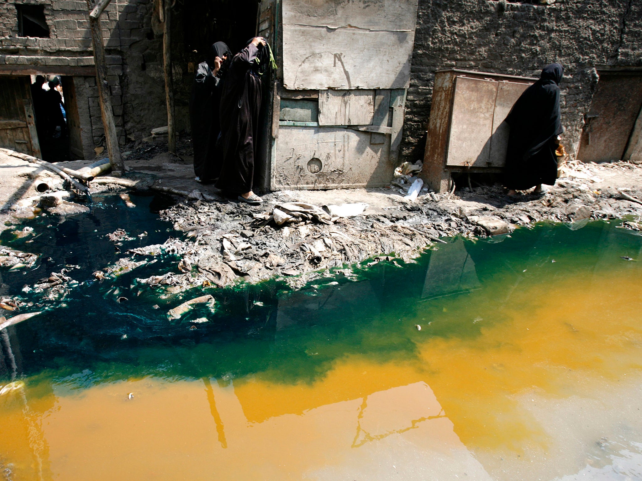 Women walk past tannery wastewater that is being pumped from a factory straight into the street, in Cairo’s Ain el-Sirra district