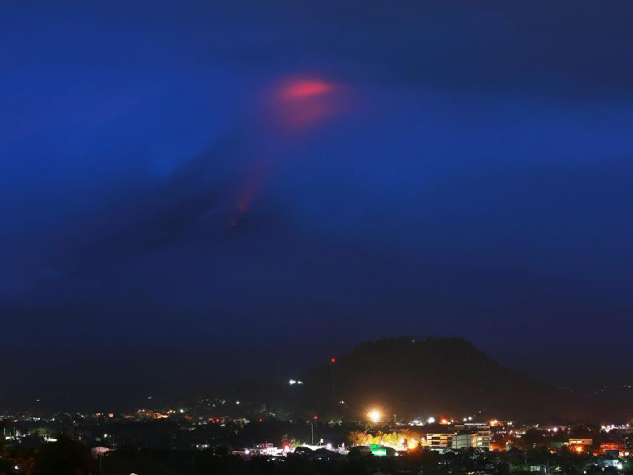 The glow (at top) of lava from the cloud-covered Mayon volcano as it erupts is pictured from the Philippine city of Legazpi in Albay province (Getty Images )