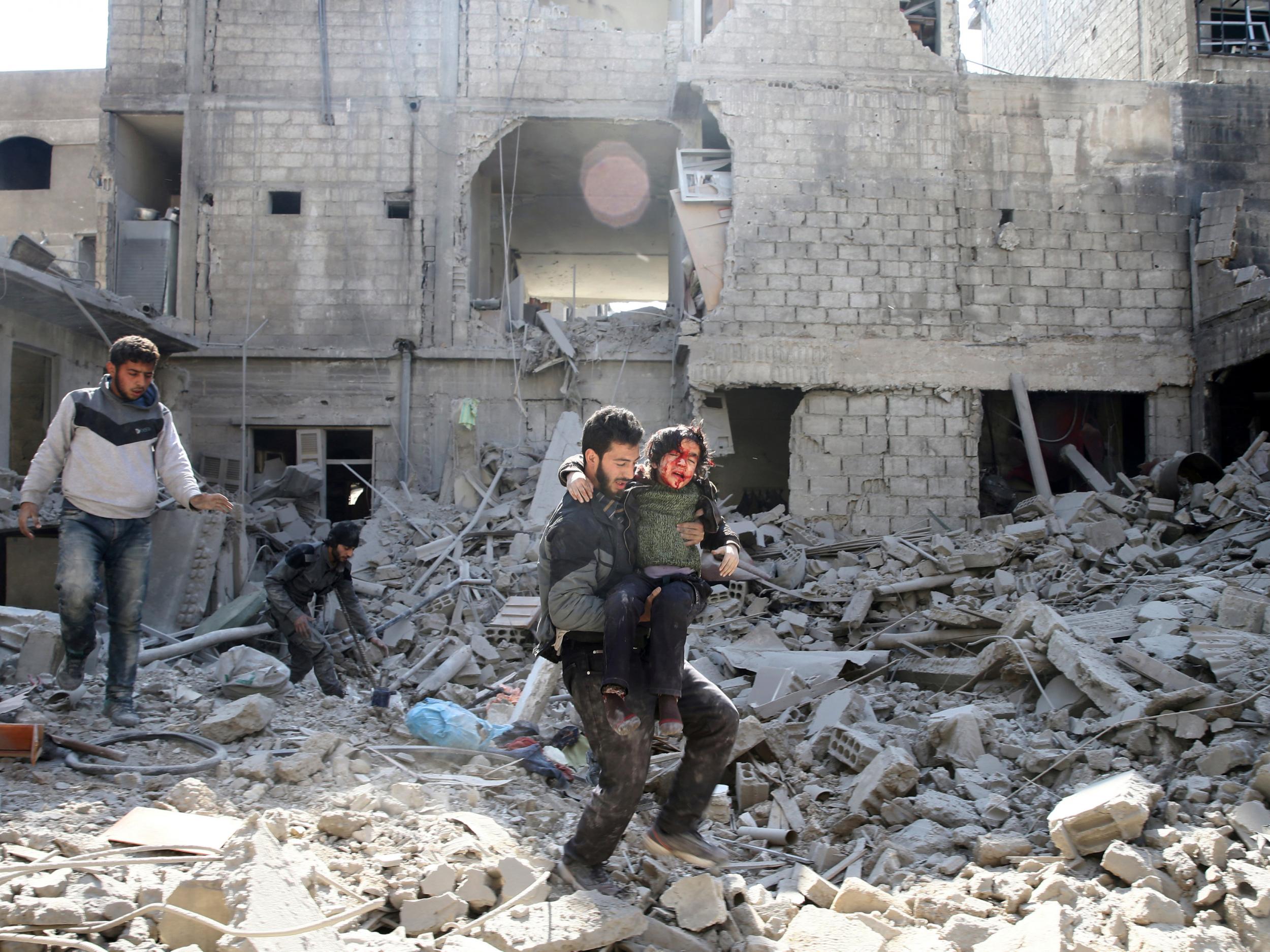 A man carries an injured boy as he walks on rubble of damaged buildings in the rebel held besieged town of Hamouriyeh, Eastern Ghouta, near Damascus (REUTERS/Bassam Khabieh)