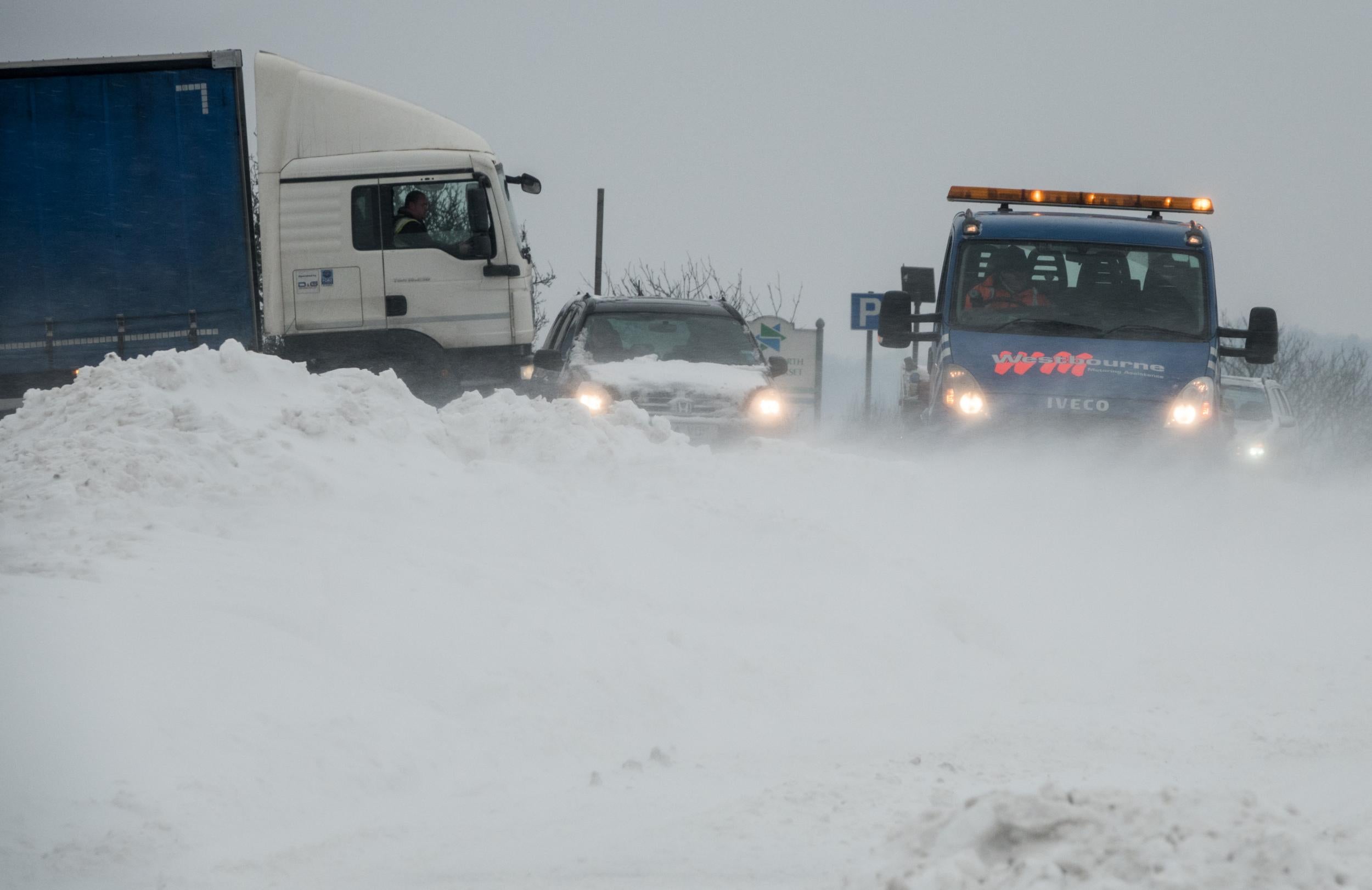 Vehicles attempt to drive through drifting snow that has formed on the A46, near Bath