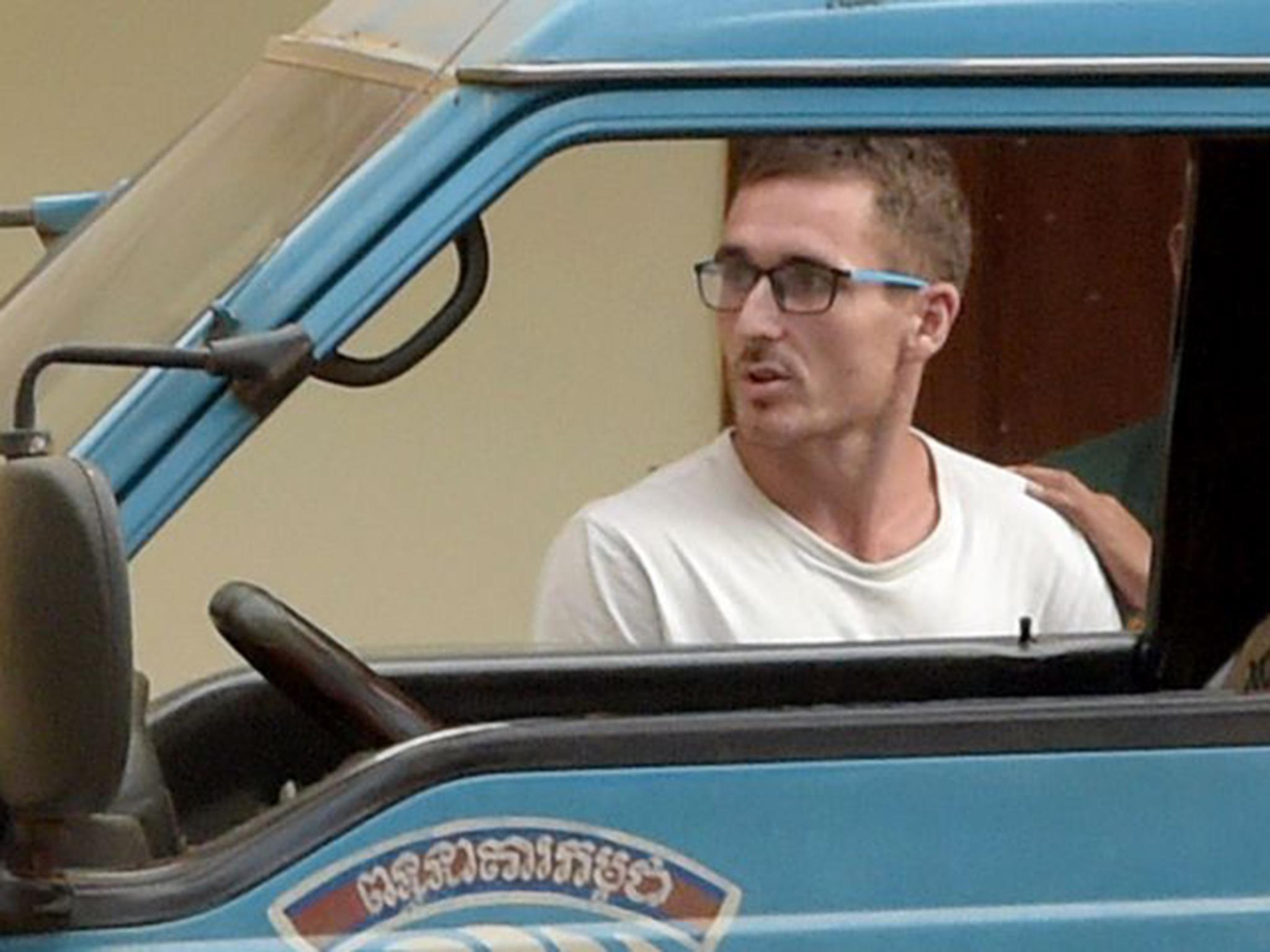 Daniel Jones, on trial for promoting a pool party with images deemed "pornographic", is escorted by a prison guard at a court in Siem Reap