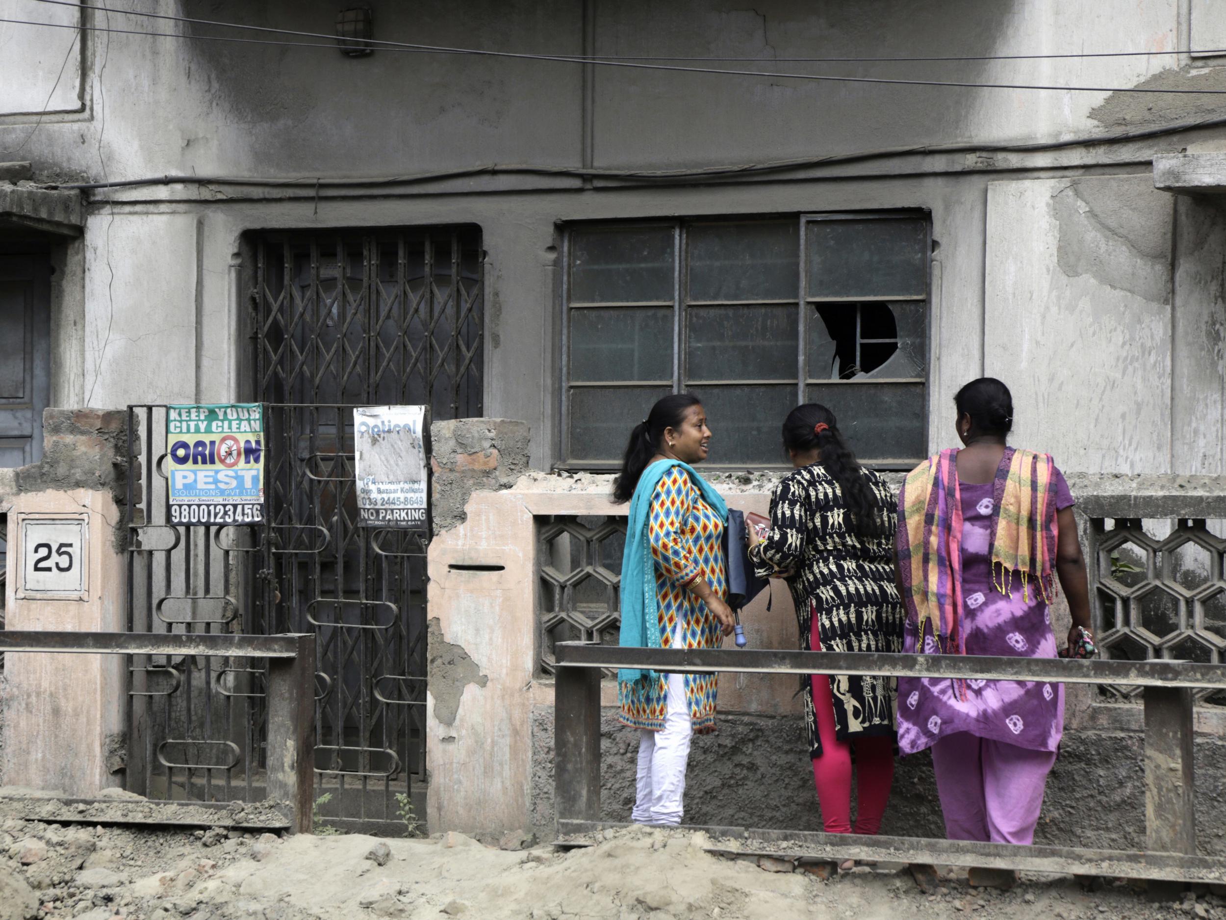 Women stand outside the house in India where 46-year-old Subhabrata Majumdar kept his mother's body in a freezer for three years