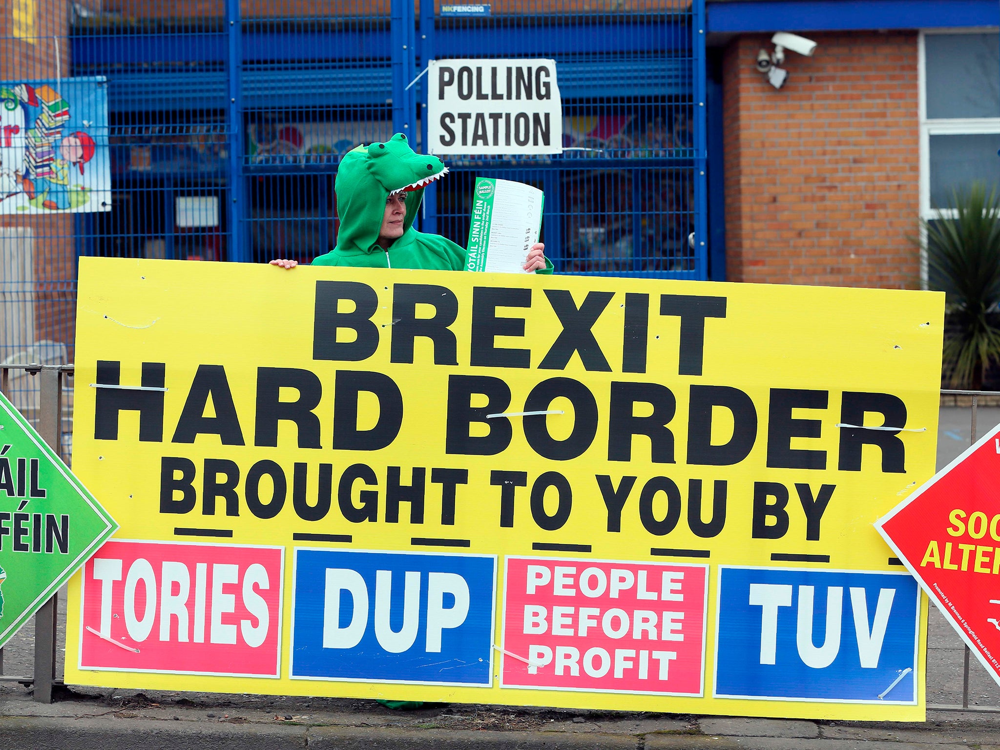 A Sinn Fein party election worker dressed up as a crocodile stands behind a banner outside a polling station in Belfast