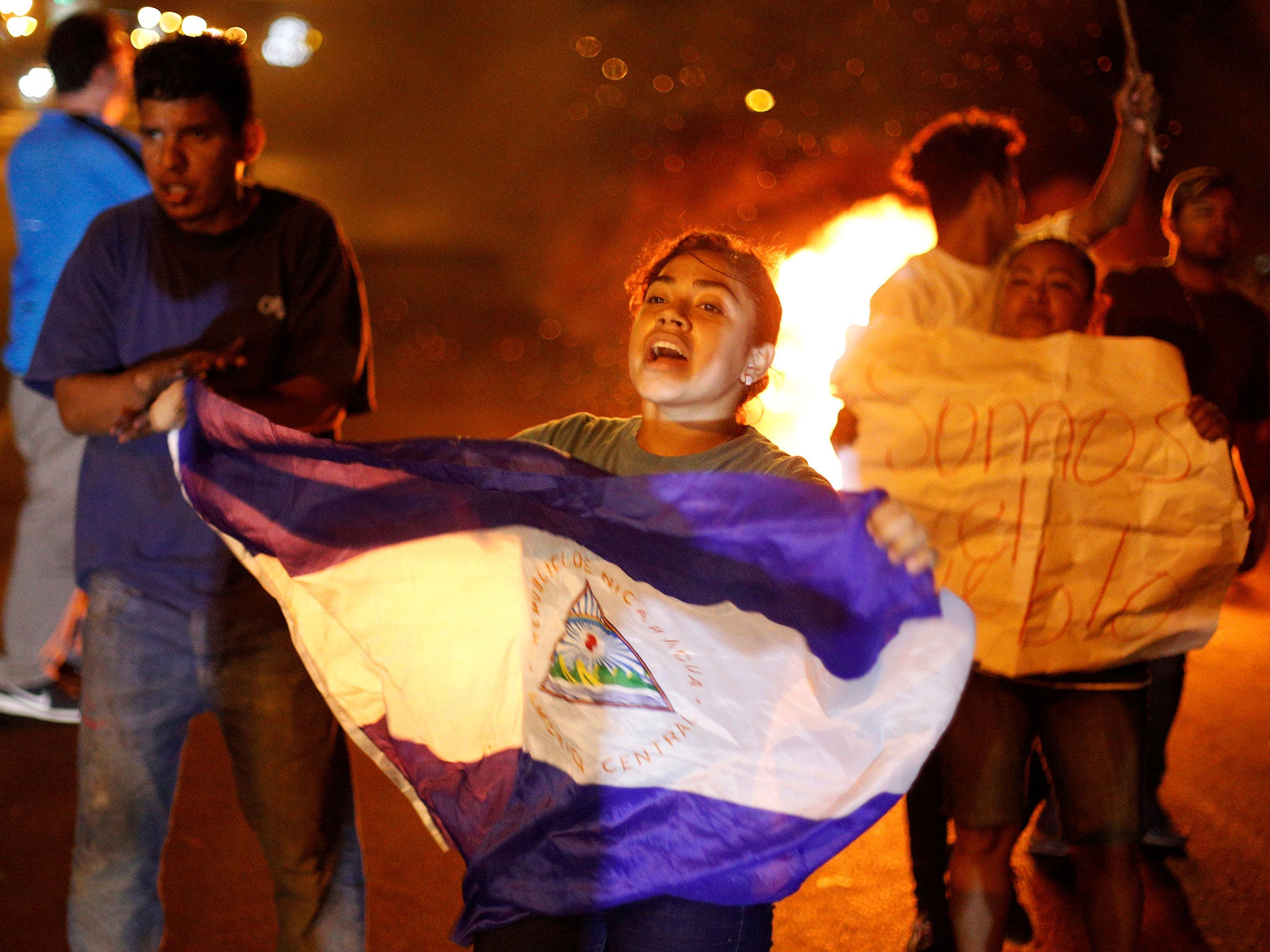 A demonstrator holds up a Nicaragua flag next to a burning barricade as demonstrators take part in a protest over a controversial reform to the pension plans of the Nicaraguan Social Security Institute (INSS) in Managua, Nicaragua