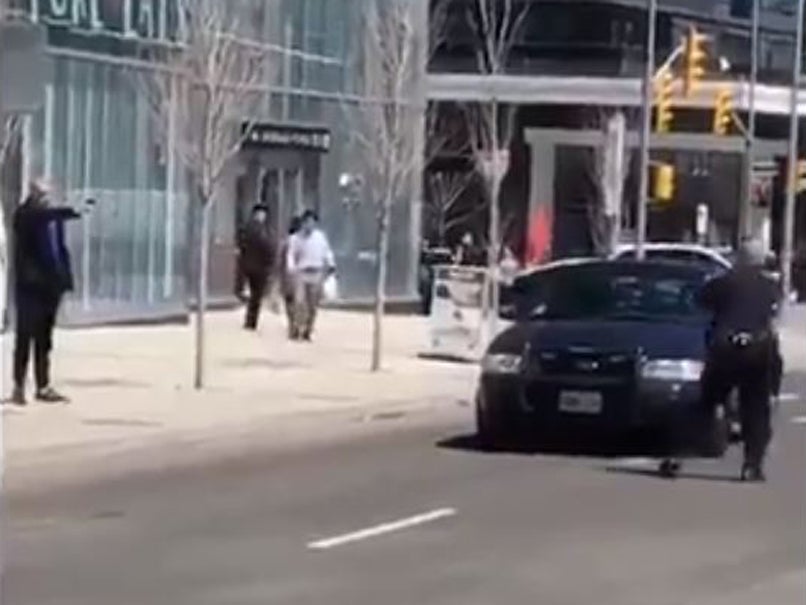 A lone police officer (R) confronts the man suspected of driving a van into pedestrians in Toronto (L) as he points an object that looks like a gun