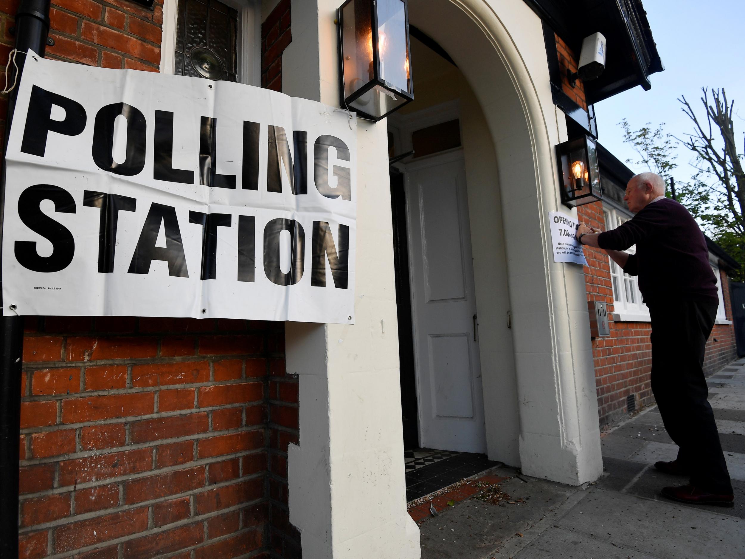 A man fixes a sign to the door of a polling station as voting begins in local government elections in London