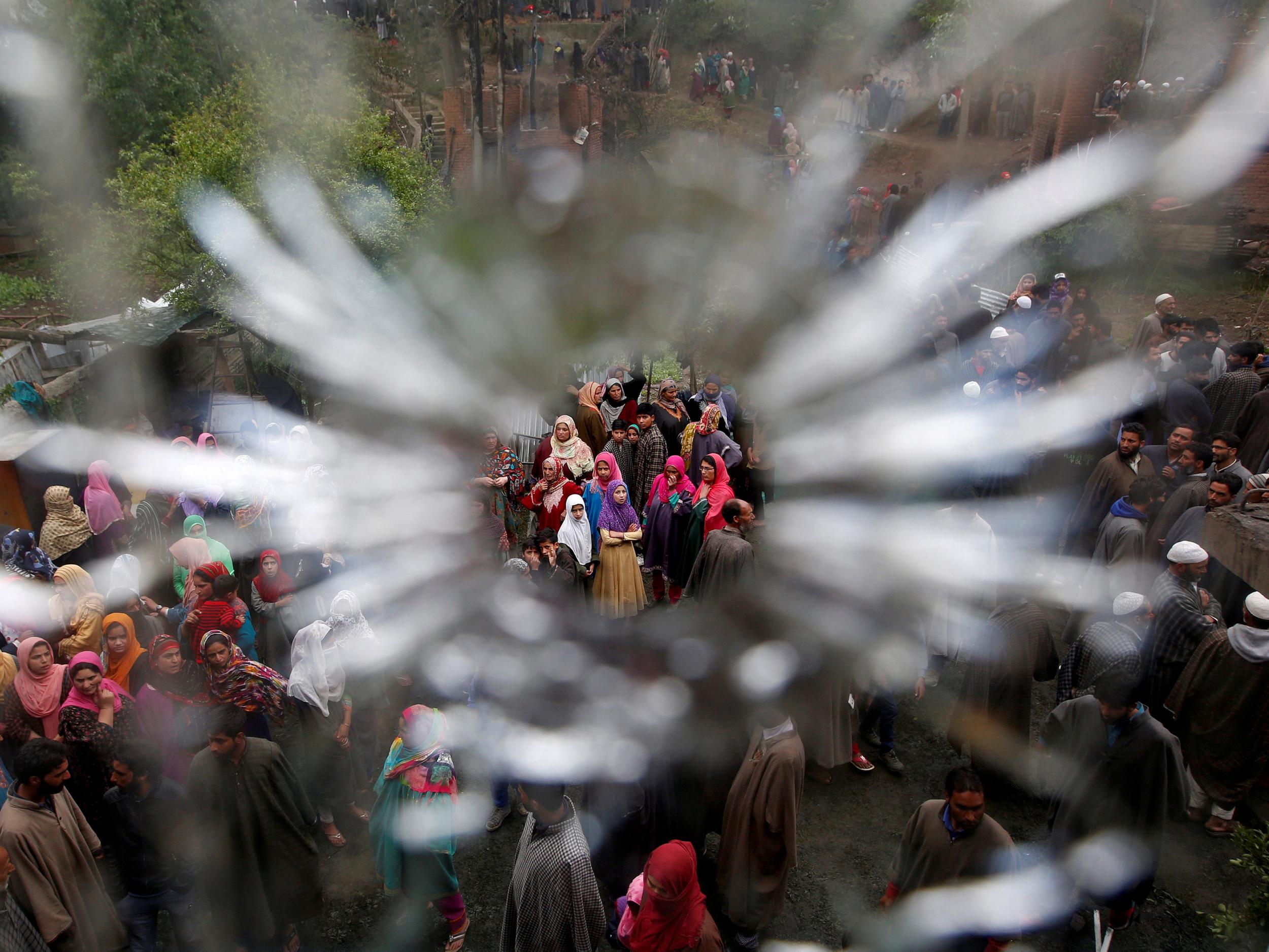 People are seen through a bullet hole in a window of a damaged house after a gun battle between suspected militants and Indian security forces at Turkewangam village in Kashmir’s Shopian district