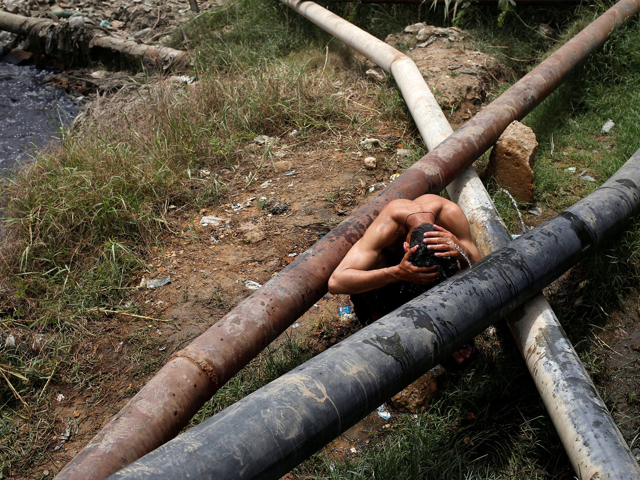 A man soaks his head in water gushing from a leaking pipe in Karachi