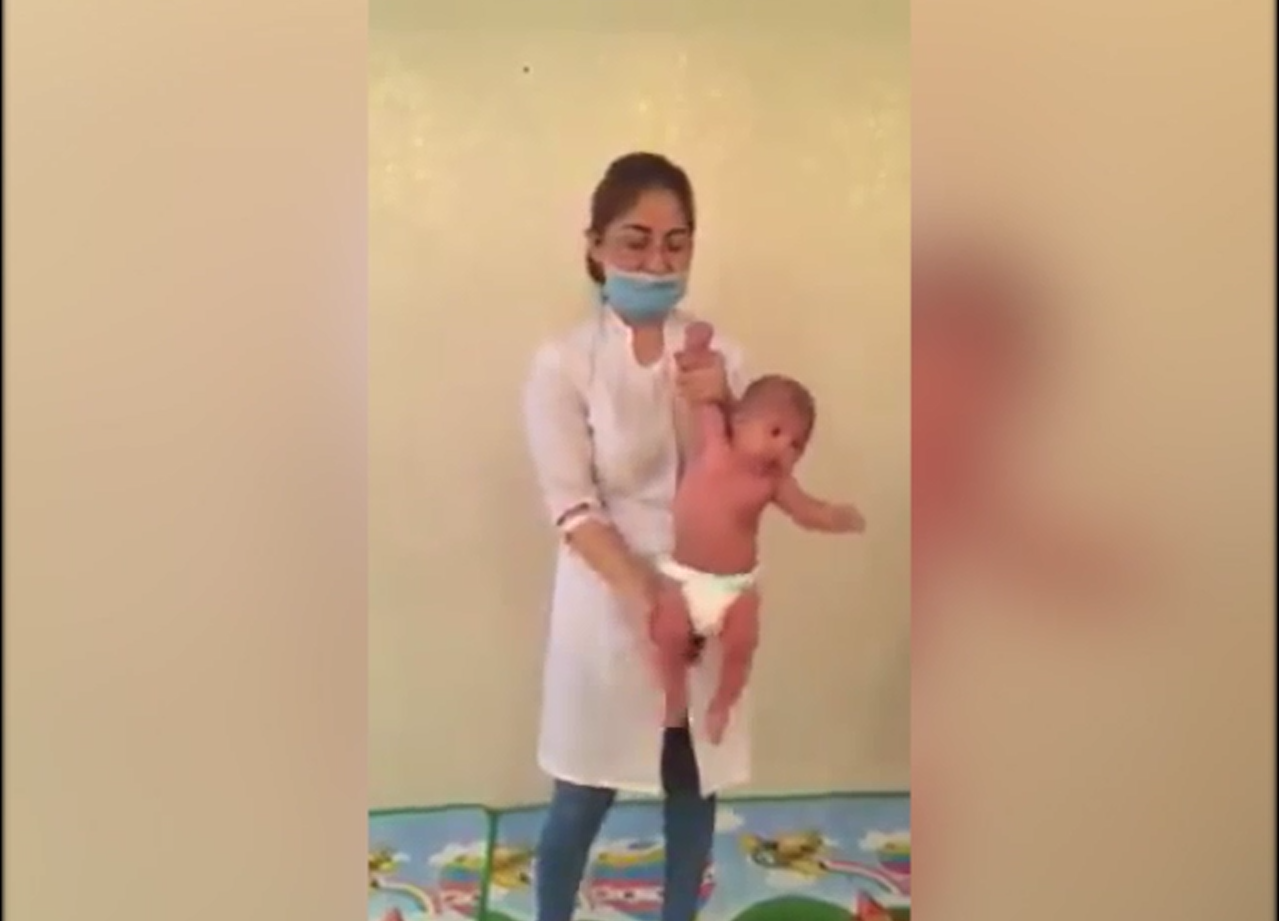 Ms Orynbasarovna holds the baby boy by his wrist as she performs a 'baby massage'