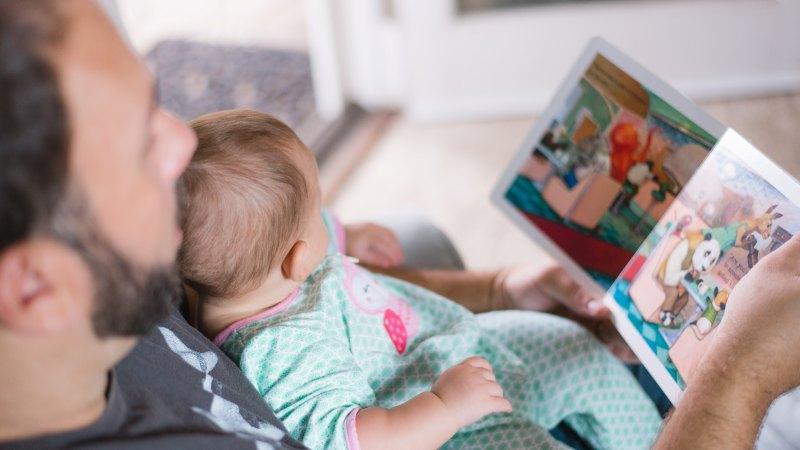 A young child rests on her father's chest while he reads her a bedtime story