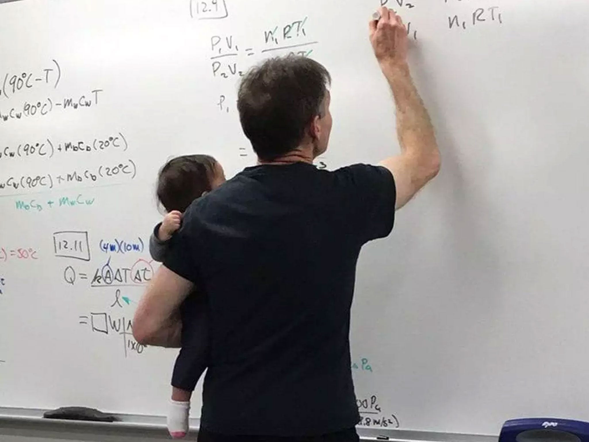 A physics lecturer holding his student's baby during a class