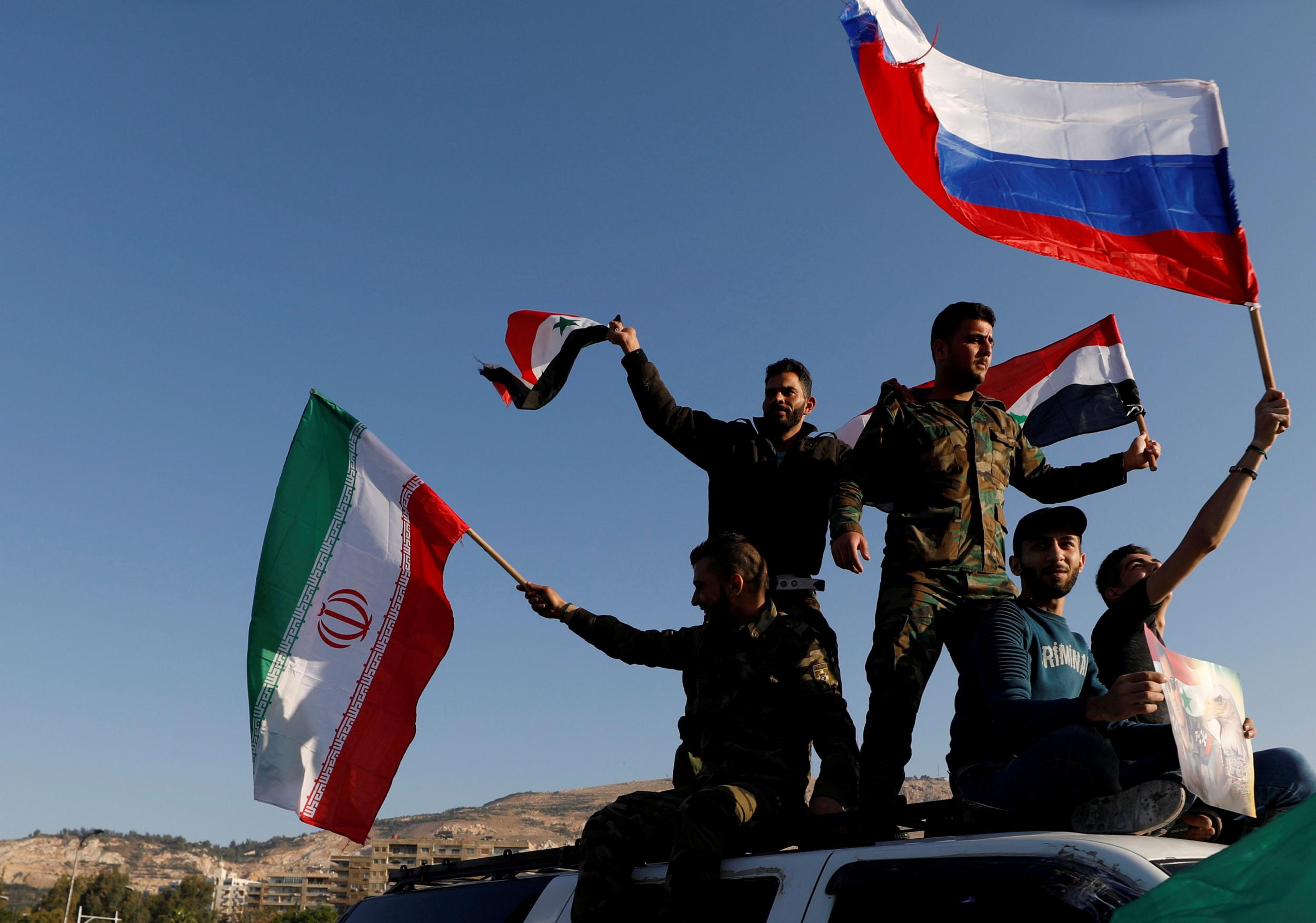 Syrians wave Iranian, Russian and Syrian flags during a 14 April 2018 protest against US-led air strikes in Damascus