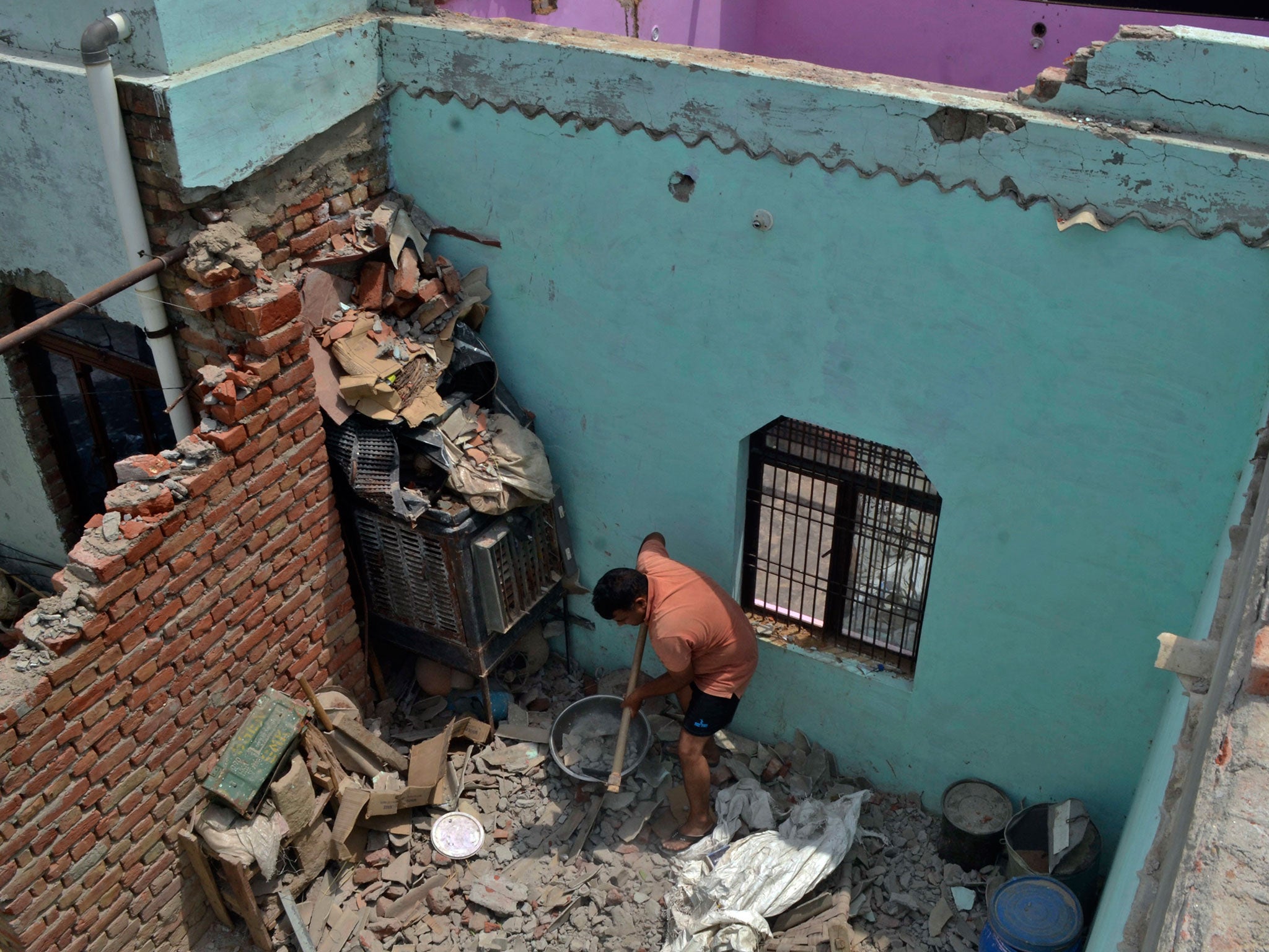 A man cleans a room littered with concrete after walls and the roof of his house collapsed during a dust storm in Uttar Pradesh in early May